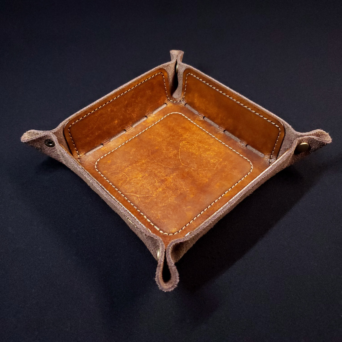 Walnut brown leather dice tray with brown stitching and bronze buttons, viewed from the top.