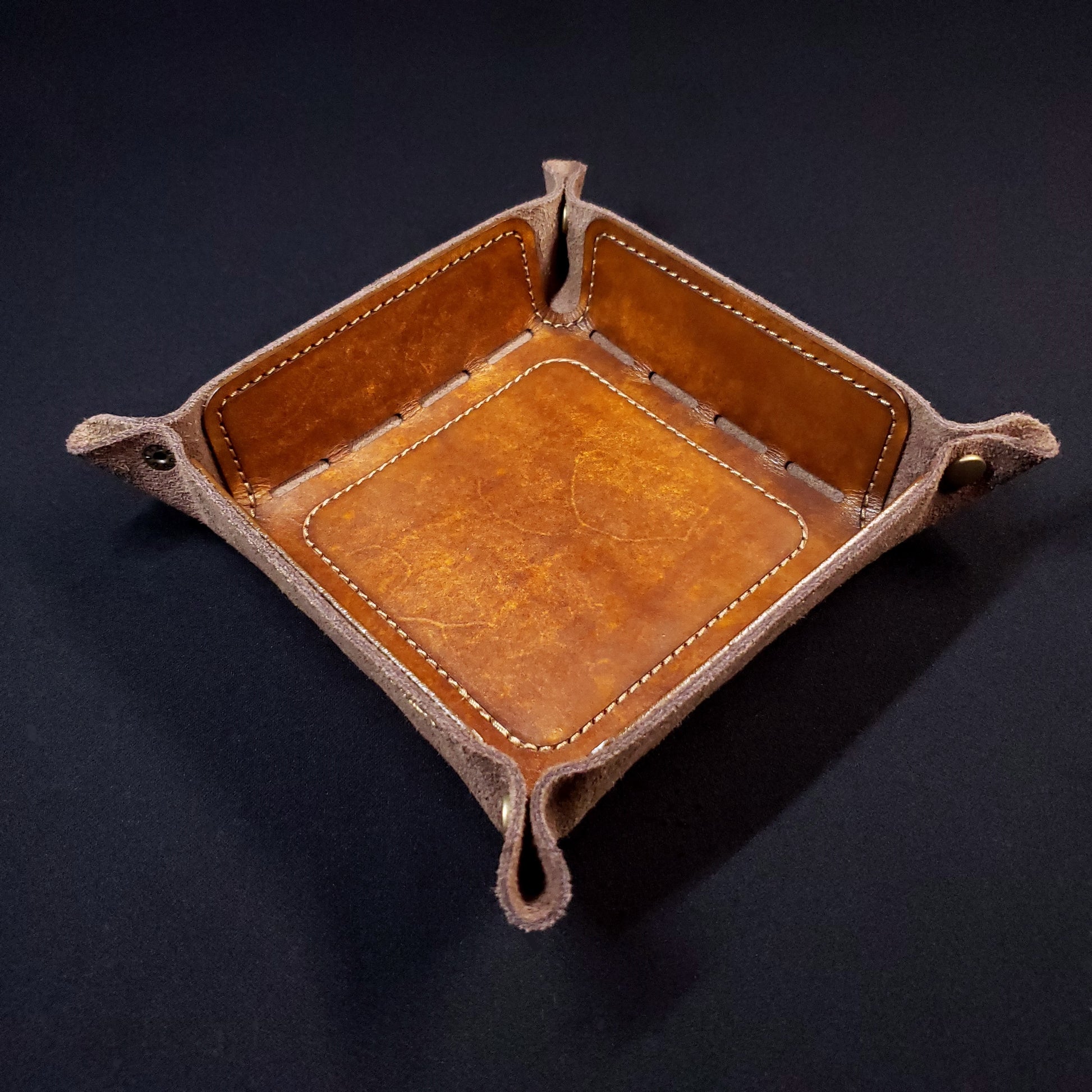 Walnut brown leather dice tray with brown stitching and bronze buttons, viewed from the top.