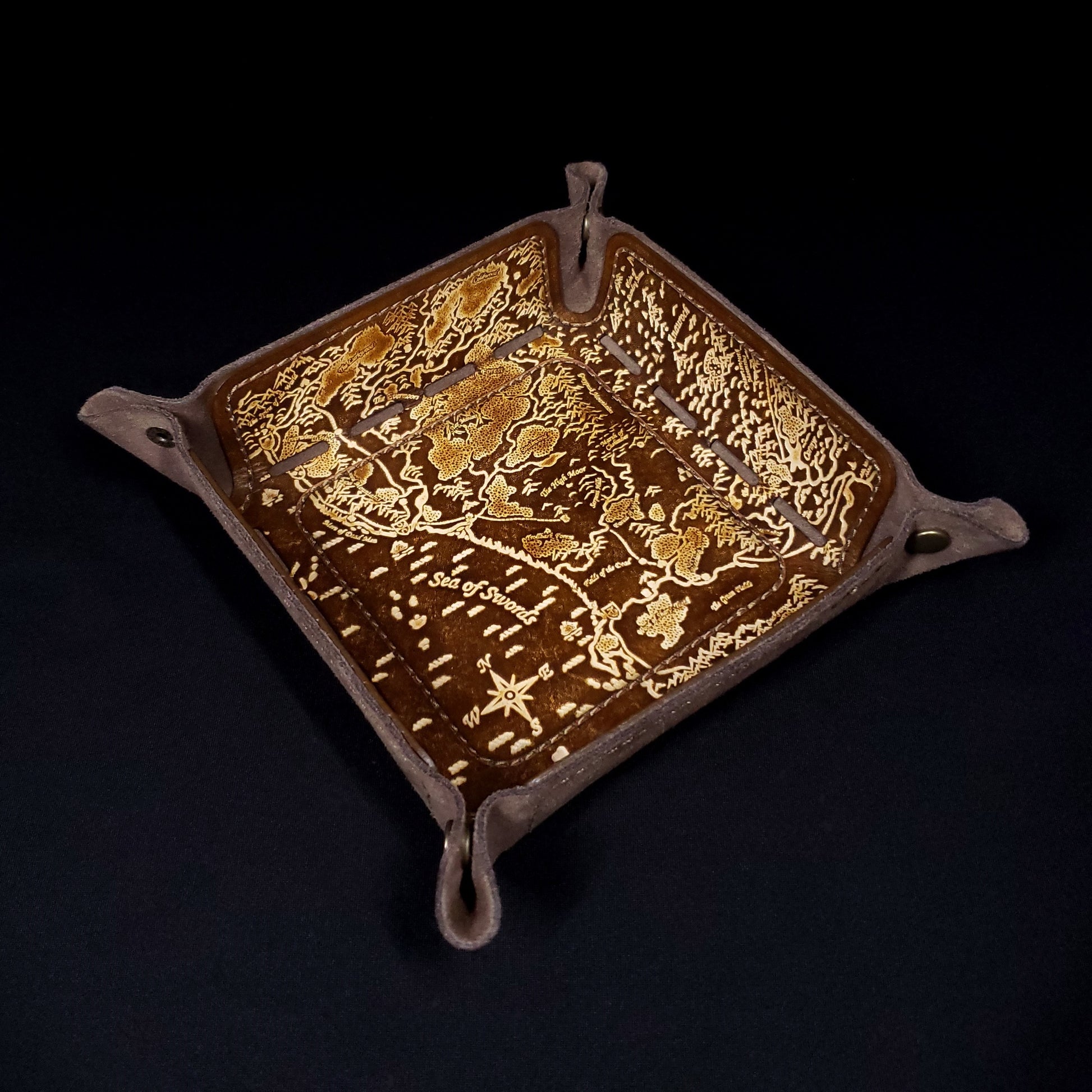 Brown leather dice tray decorated with a fantasy map of the sword coast, viewed from the top.
