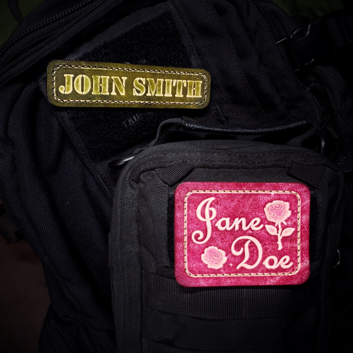 Black bag with green 'John Smith' patch on top and pink 'Jane Doe' patch below