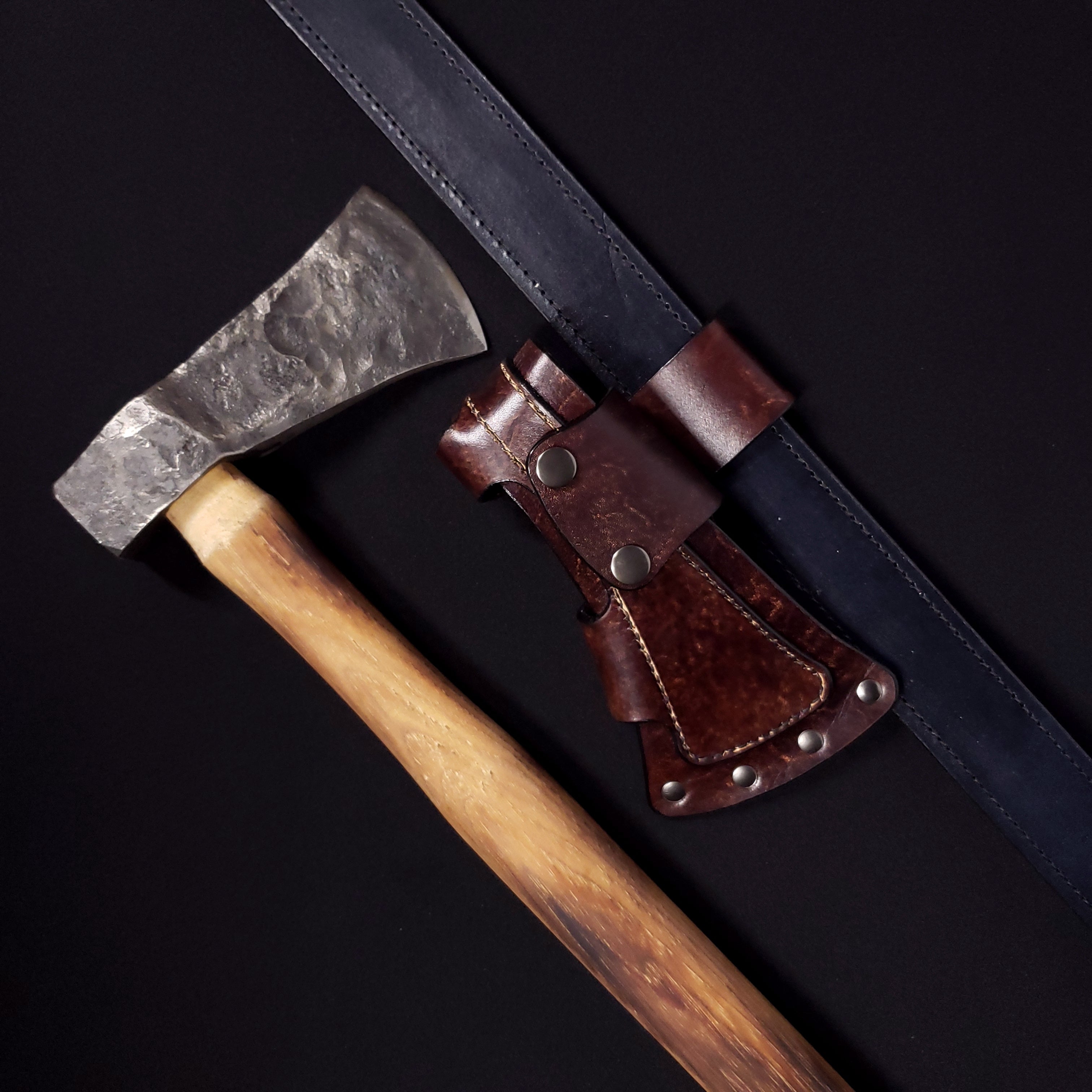 A hand axe with a brown leather sheath affixed to a belt