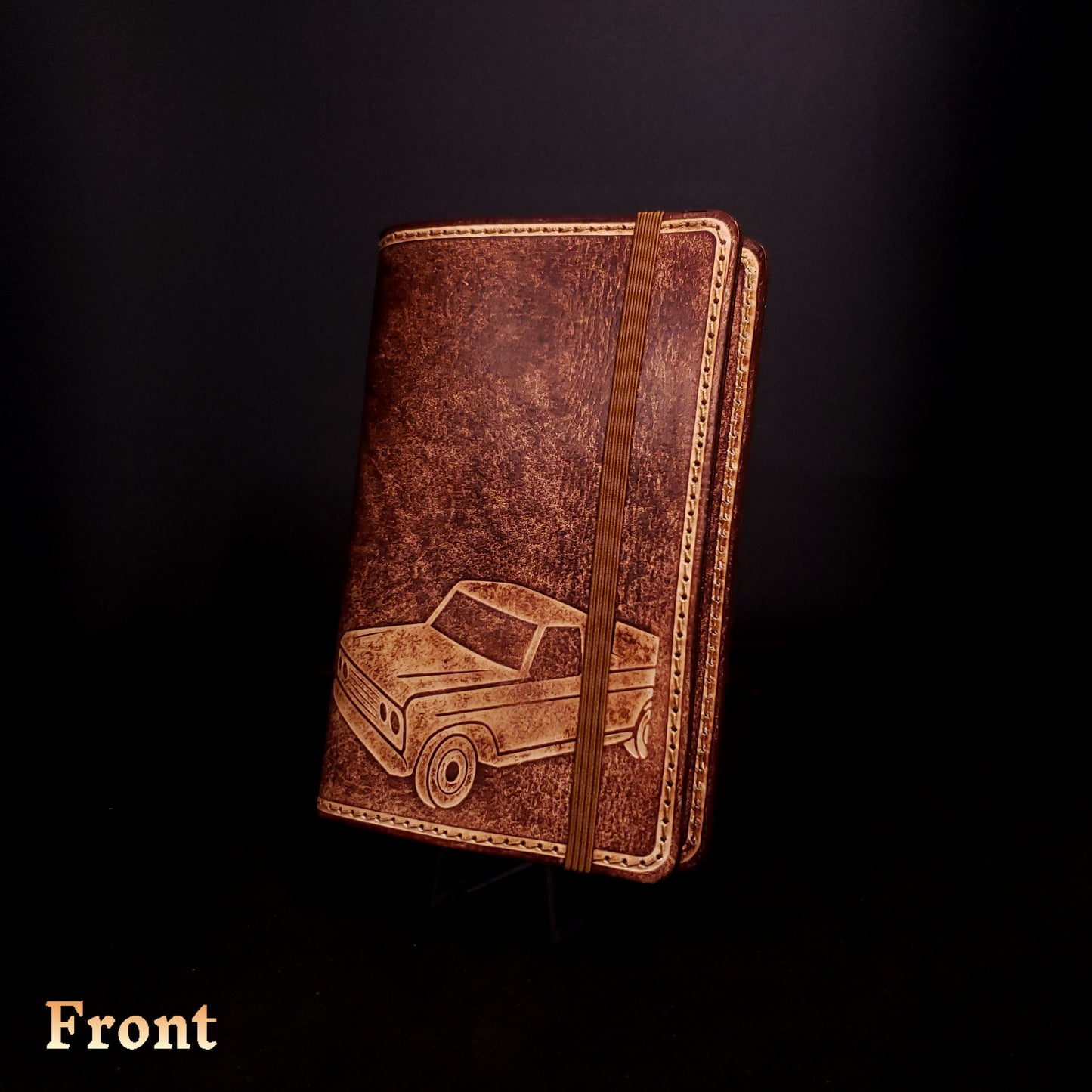 Brown leather notebook cover that's embossed with a pick-up truck and closed with an elastic strap.