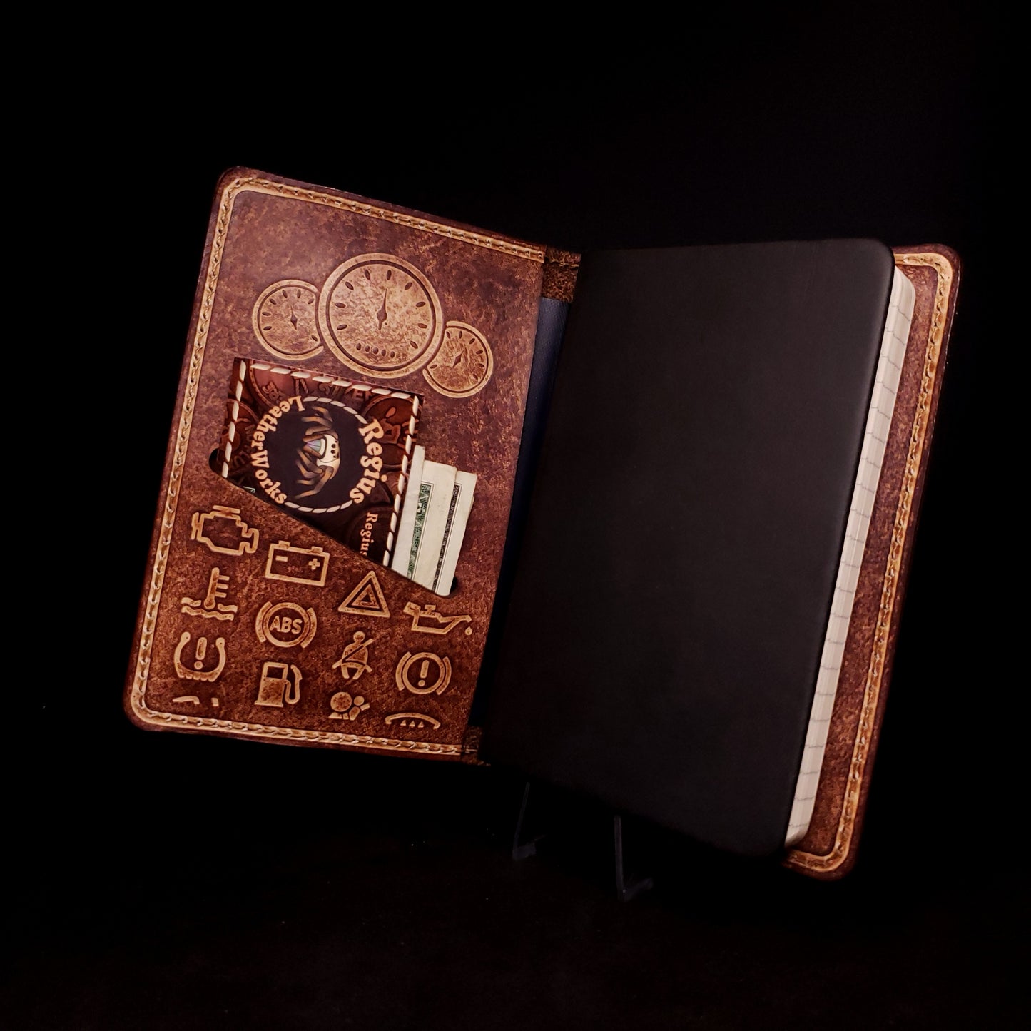 Brown leather notebook cover holding a pocket journal, embossed with a set of gauges and dash board warning lights.