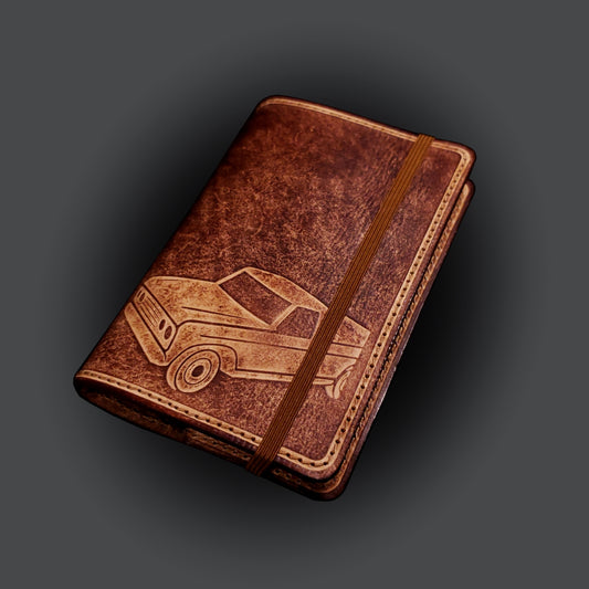 Brown leather notebook cover that's embossed with a pick-up truck, closed with an elastic strap.