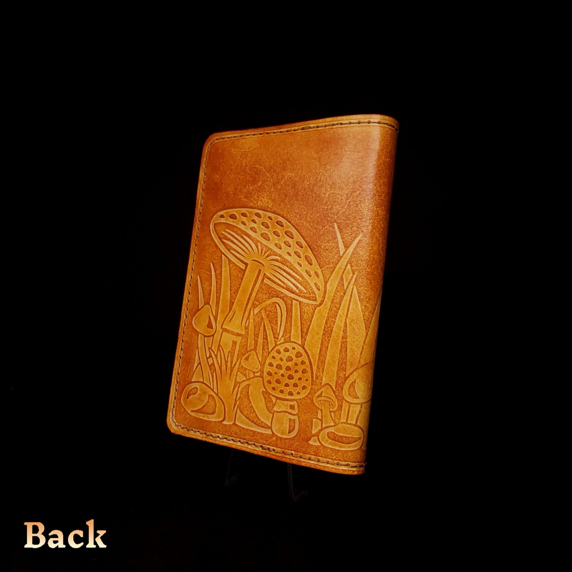Brown leather notebook cover that's embossed with a mushroom design, viewed from the back.