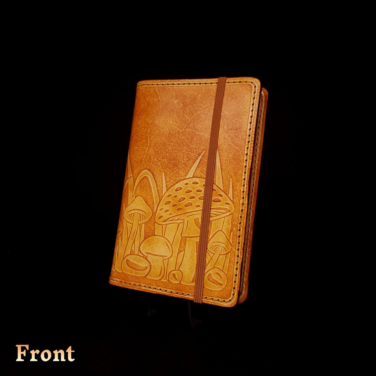 Brown leather notebook cover that's embossed with a mushroom design and closed with an elastic strap.