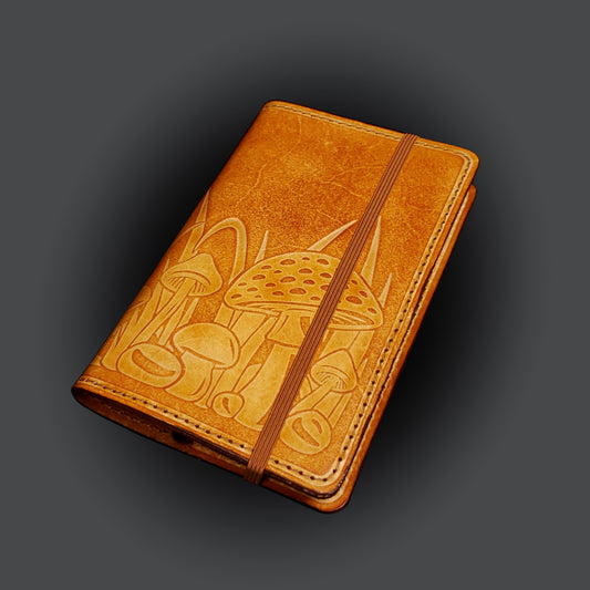 Brown leather notebook cover that's embossed with a mushroom design and closed with an elastic strap.