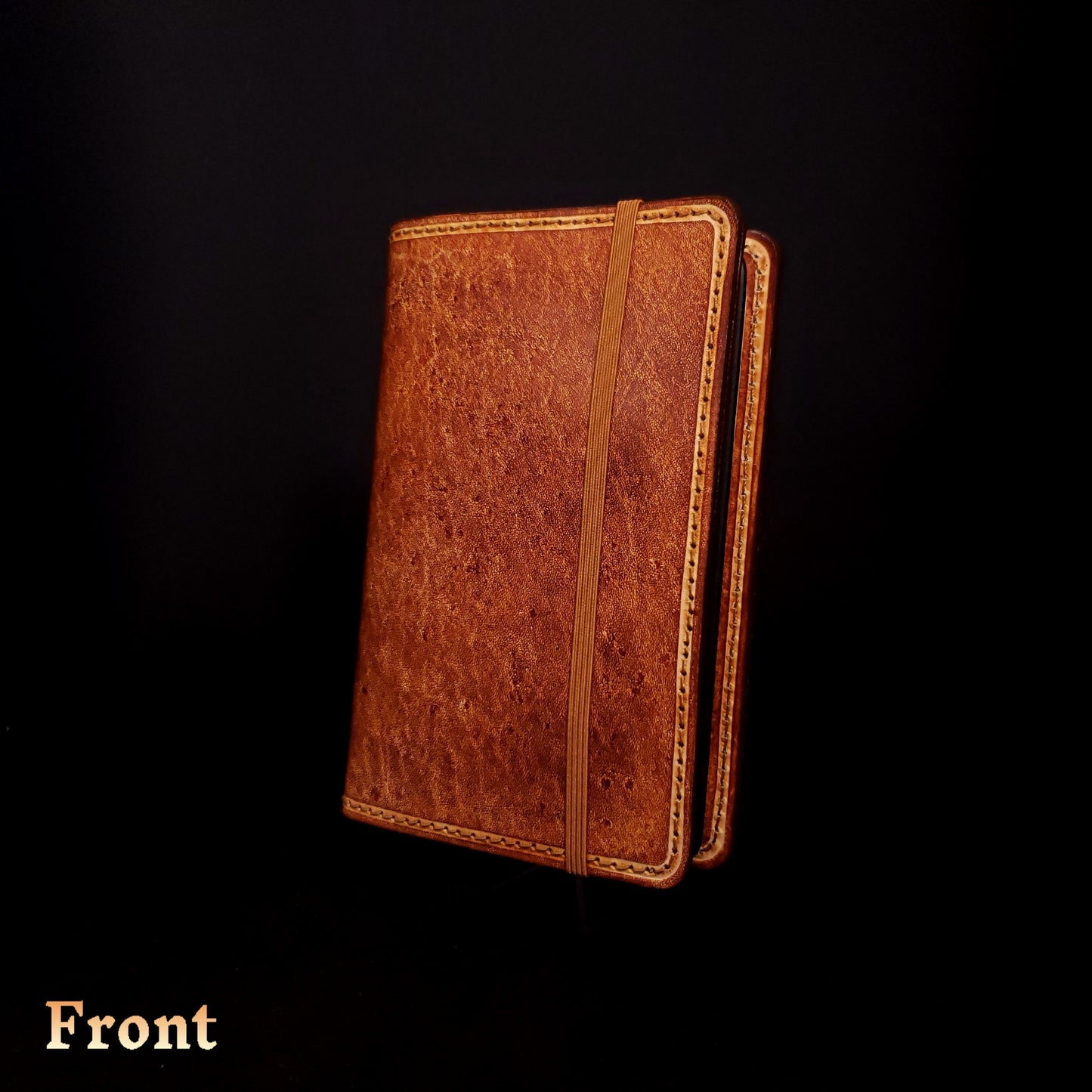 Brown leather notebook cover, closed with an elastic strap, viewed from the front.