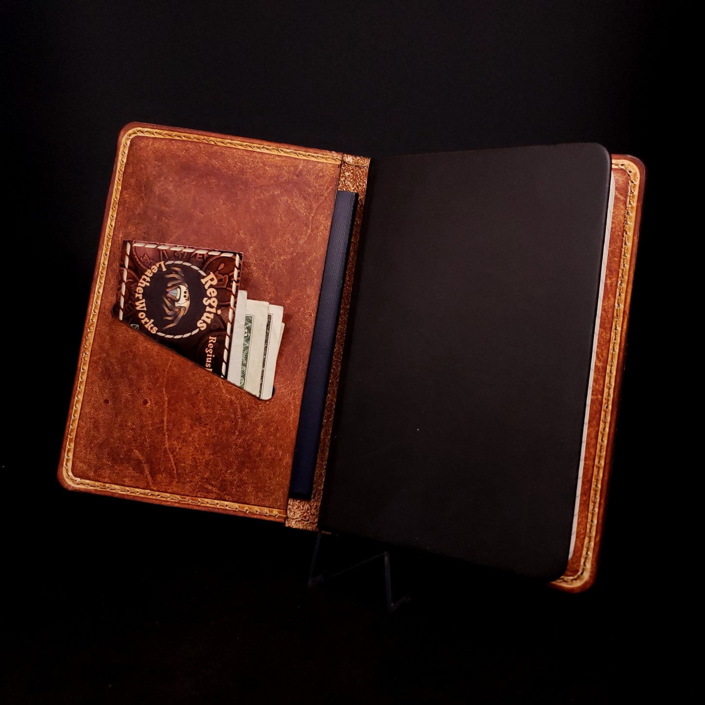 Brown leather notebook cover holding a pocket journal in its right side and money in its left side pocket.