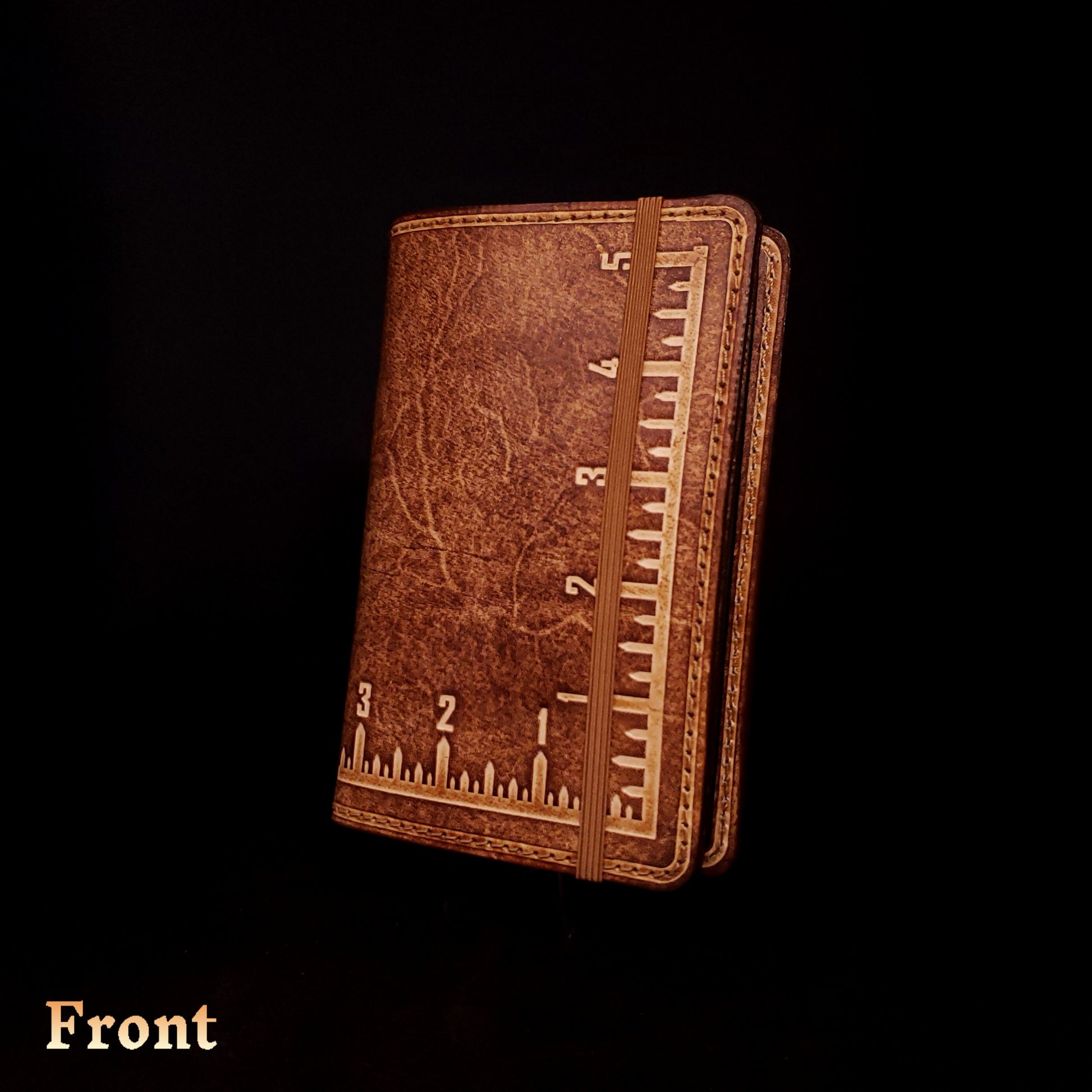 Brown leather notebook cover that's embossed with an imperial measuring square and closed with an elastic strap.