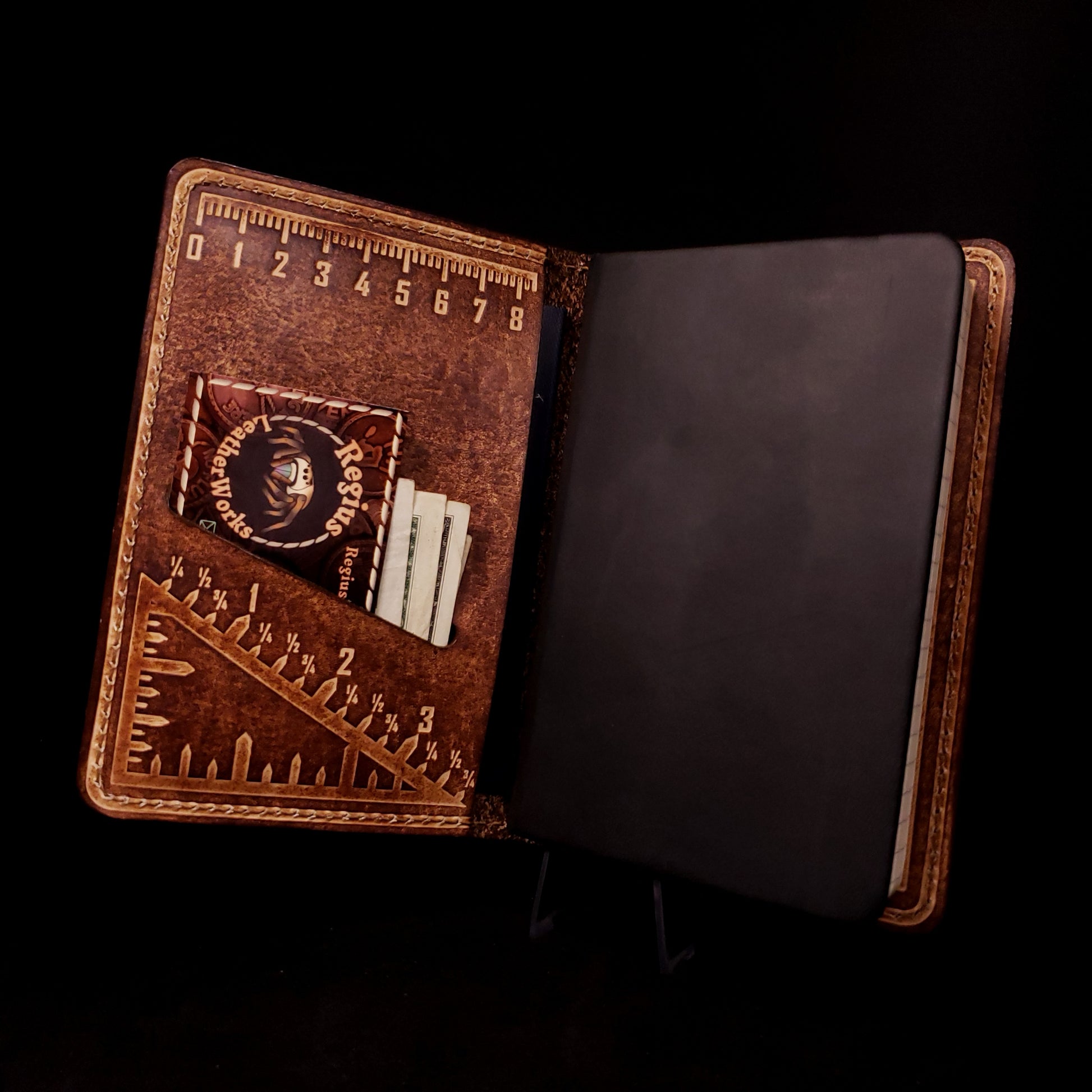 Brown leather notebook cover holding a pocket journal, embossed with a metric ruler and imperial triangle measuring square.