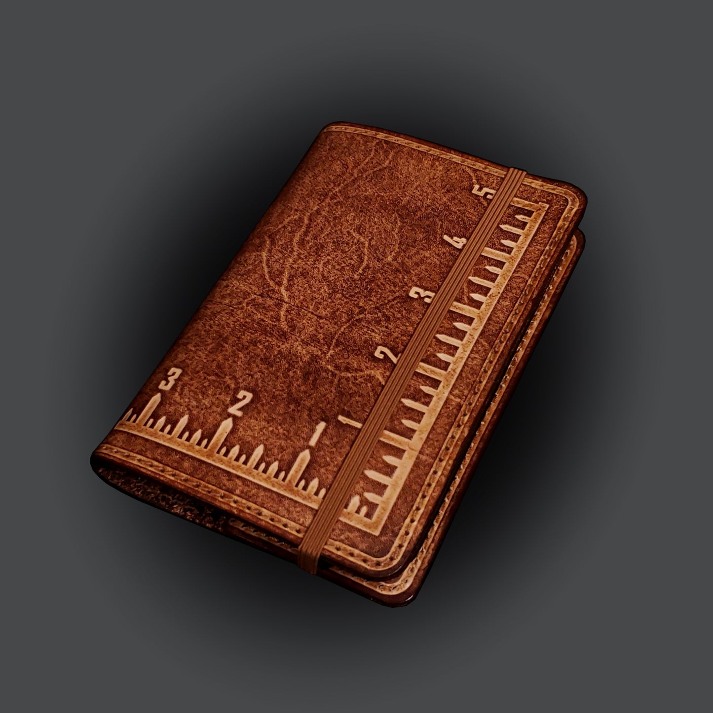 Brown leather notebook cover that's embossed with an imperial measuring square, closed with an elastic strap.