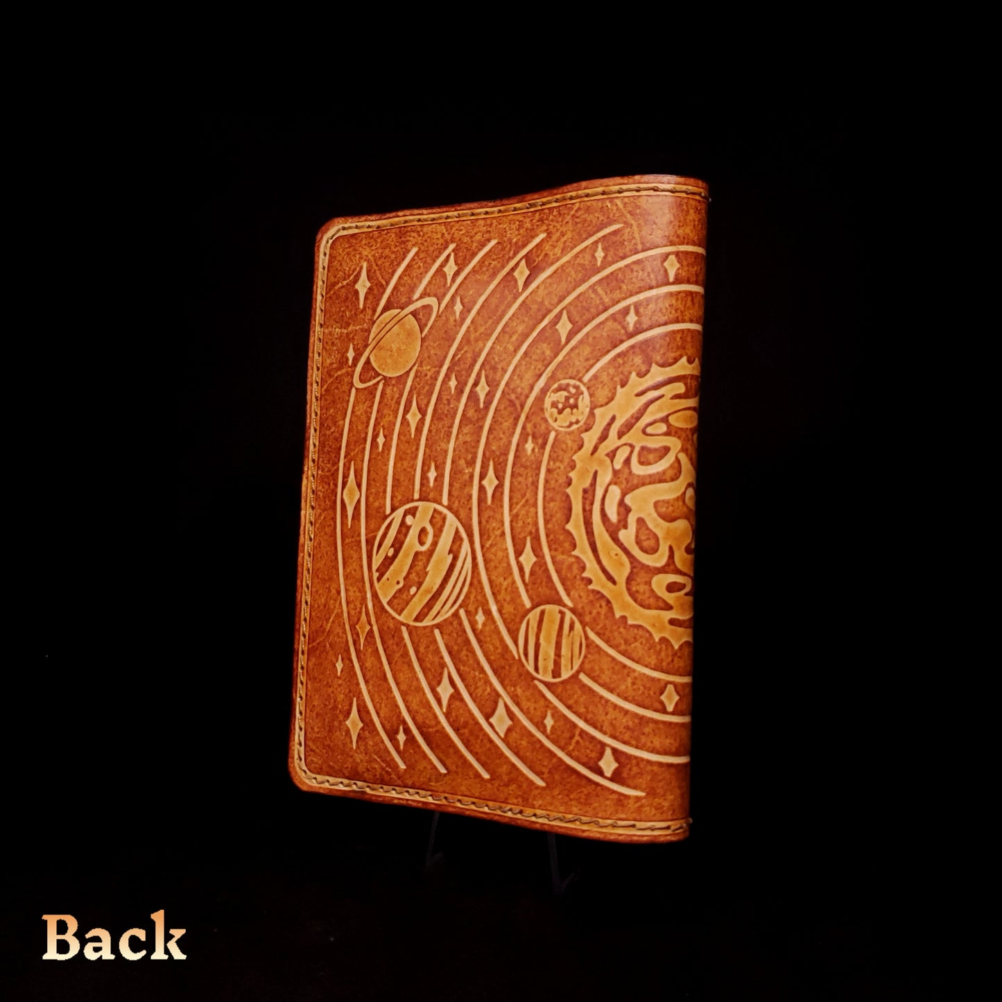 Brown leather notebook cover that's embossed with the solar system, viewed from the back.