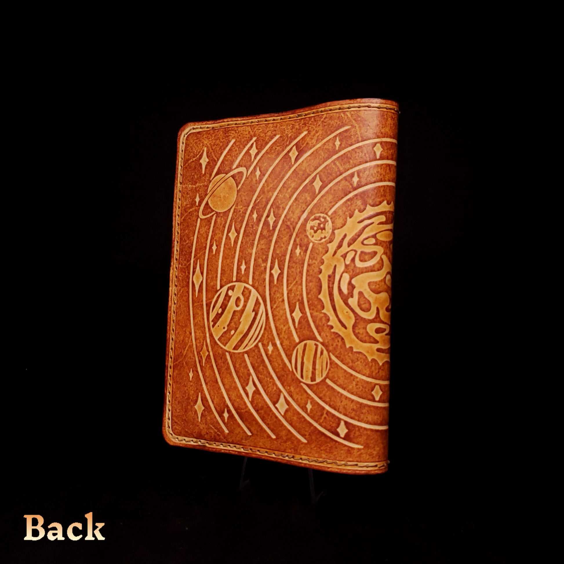 Brown leather notebook cover that's embossed with the solar system, viewed from the back.