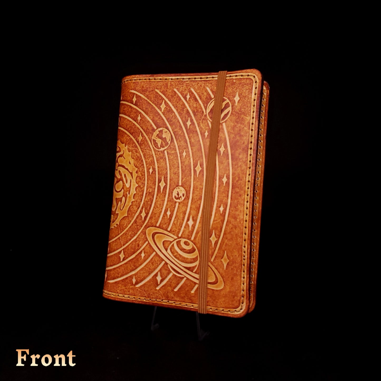 Brown leather notebook cover that's embossed with the solar system and closed with an elastic strap.