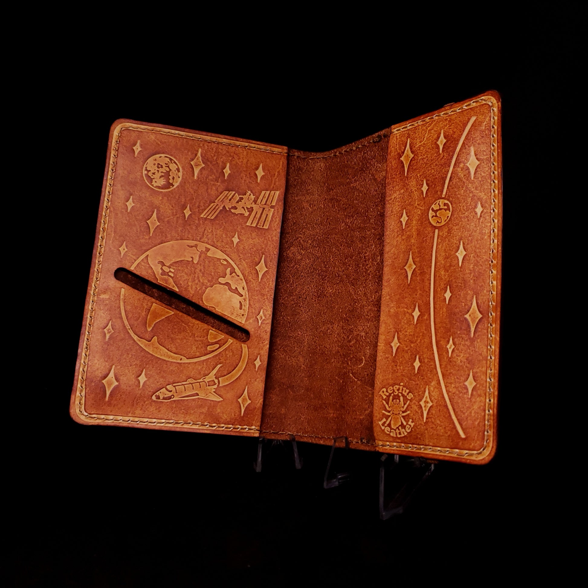 Brown leather notebook cover with a card slot and embossed with planets, a satellite, and a space shuttle.