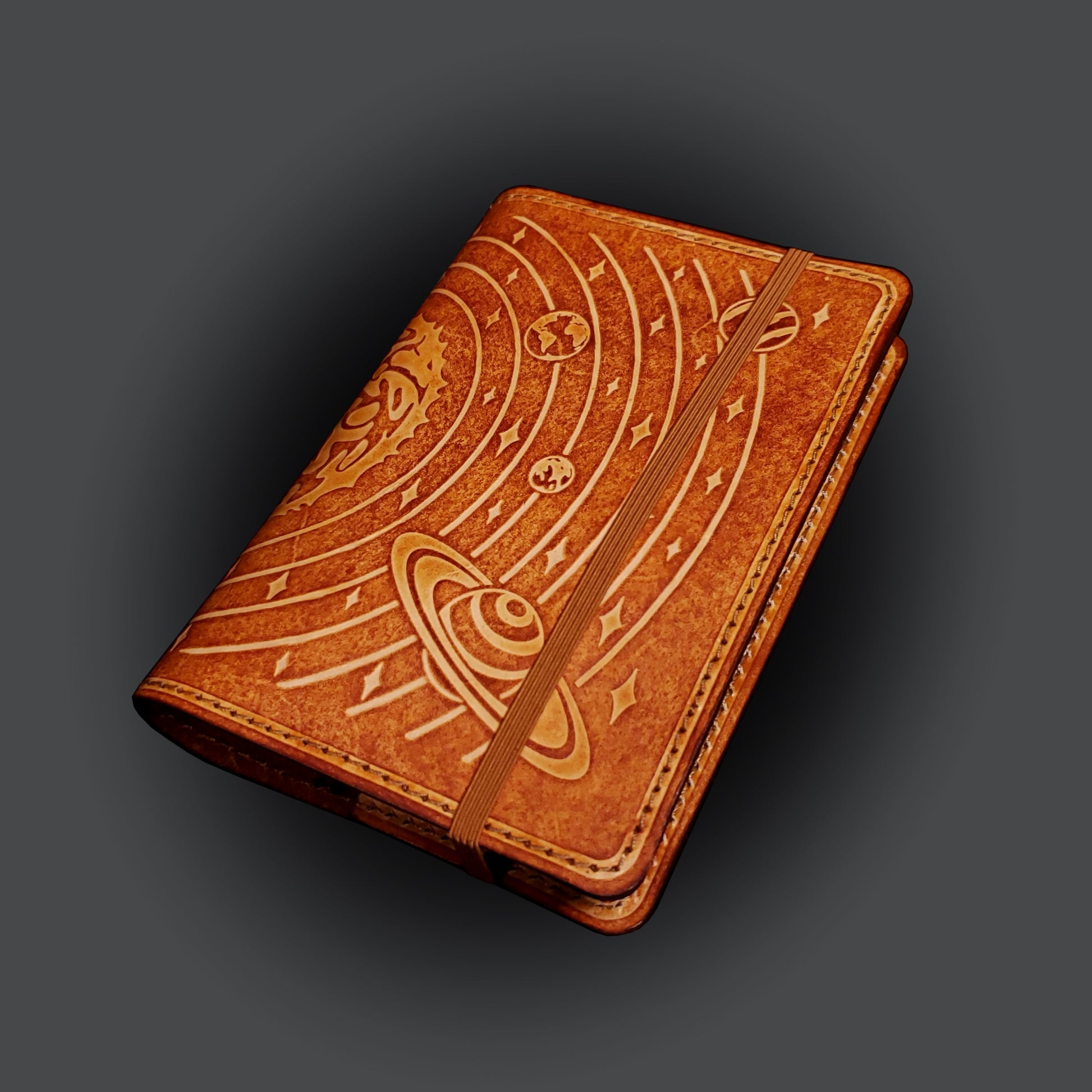 Brown leather notebook cover that's embossed with the solar system, closed with an elastic strap.