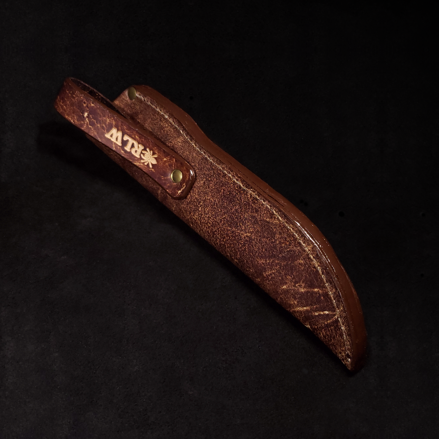 Brown leather knife sheath with a glossy edge and belt loop embossed with the Regius logo.