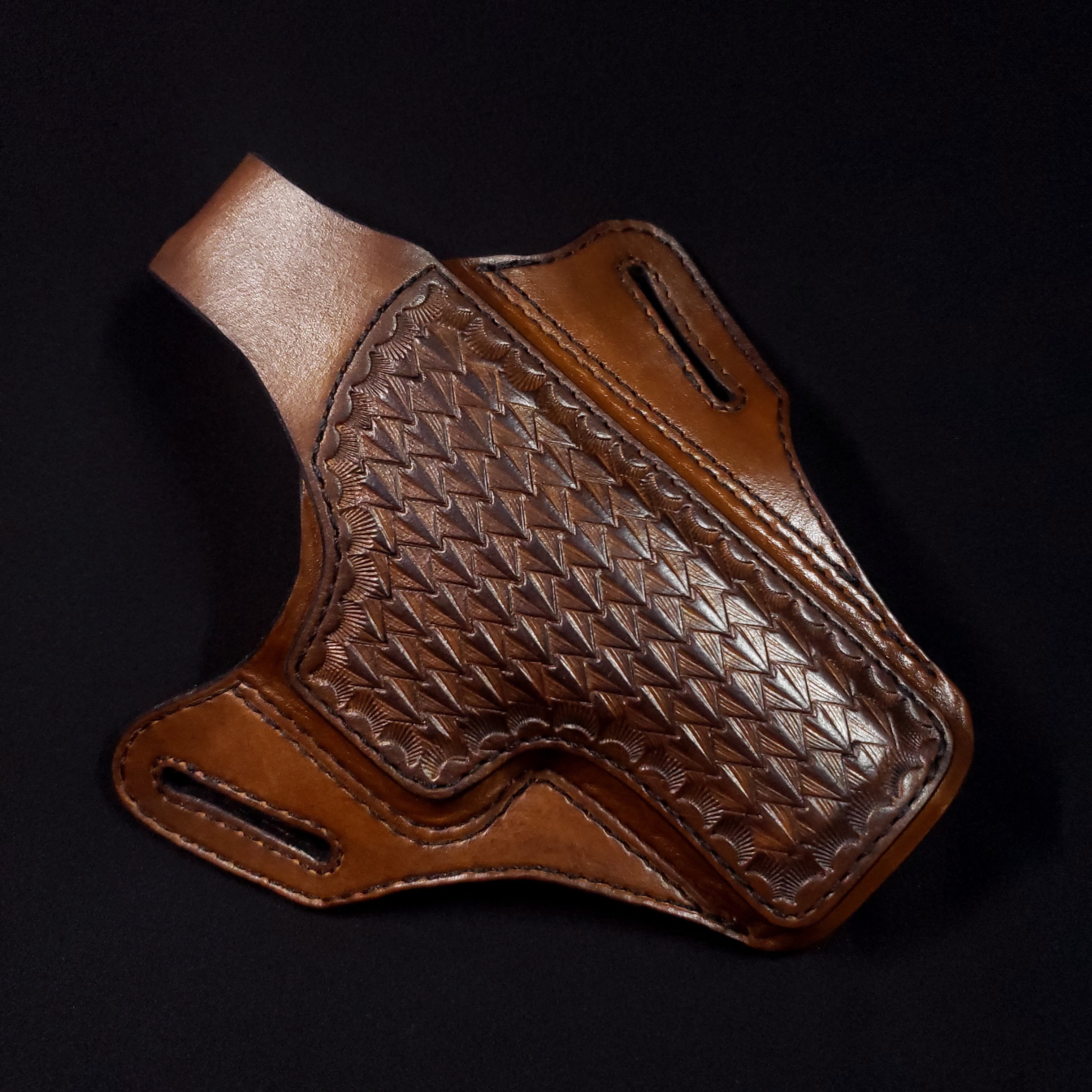 A brown leather gun holster with intricate embossing on a black background