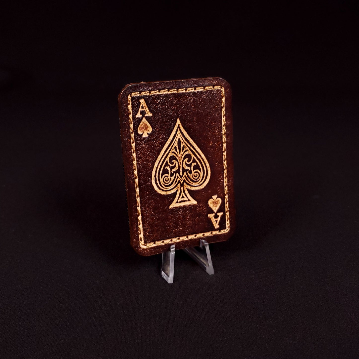 Brown rectangular velcro patch embossed to resemble an ace of spades playing card, posed on a black background.