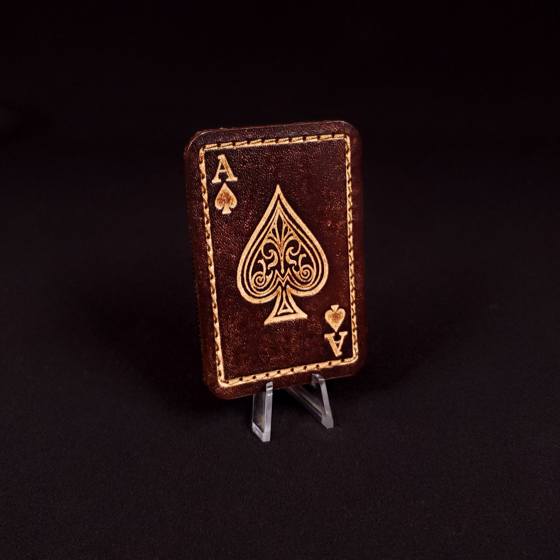 Brown rectangular velcro patch embossed to resemble an ace of spades playing card, posed on a black background.