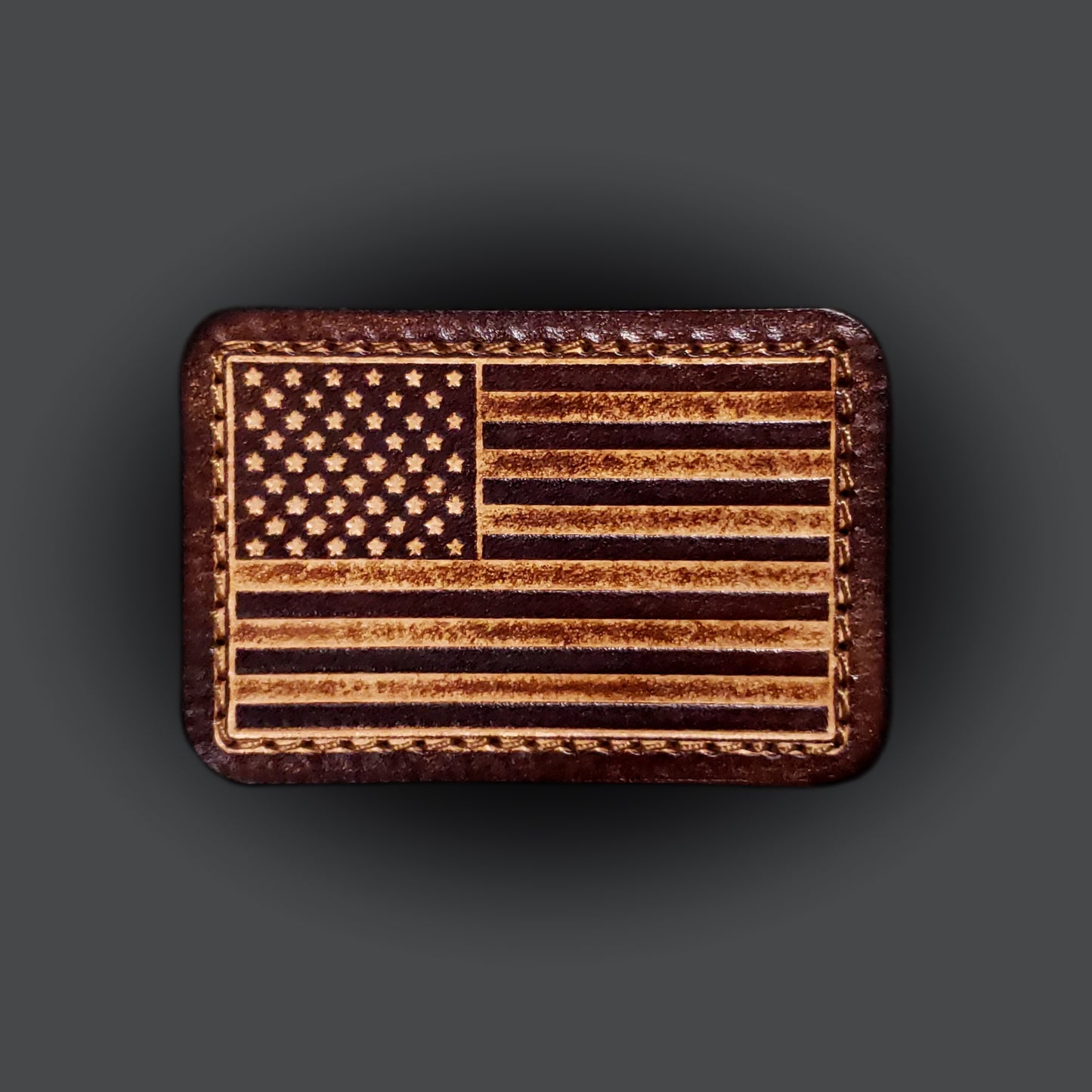 Brown rectangular velcro patch embossed with the American flag, on a grey background.