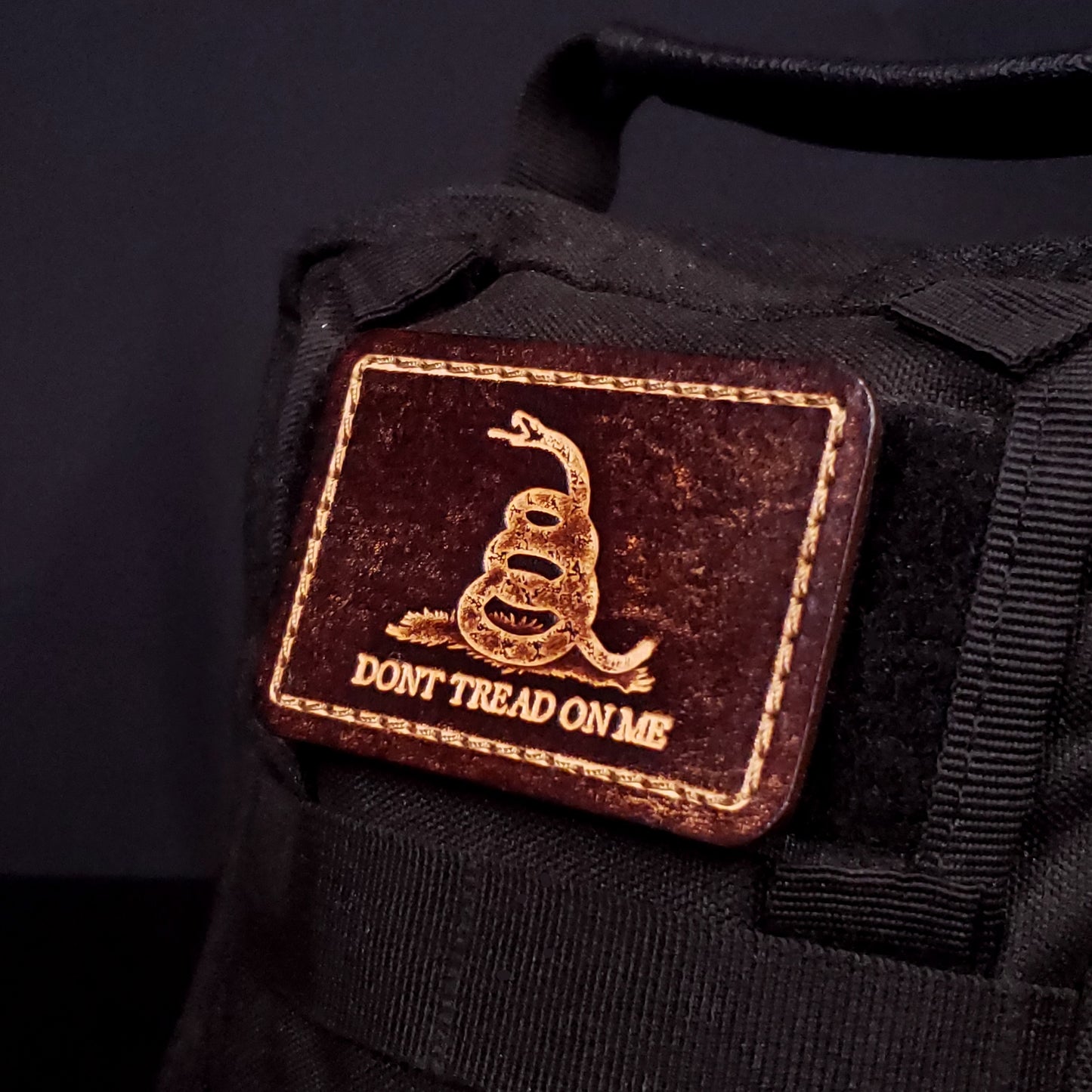 Brown rectangular velcro patch embossed to resemble the gadsden flag, affixed to a bag.