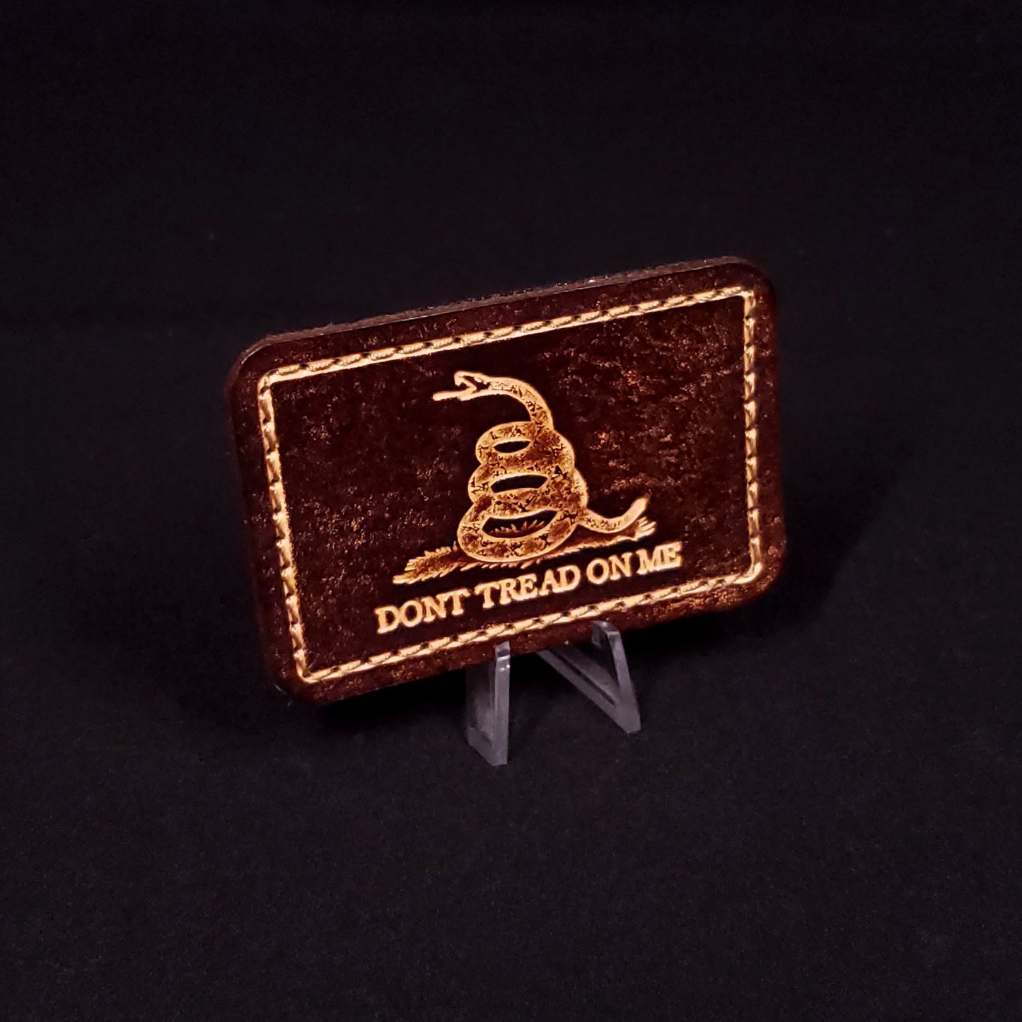 Brown rectangular velcro patch embossed to resemble the gadsden flag, posed on a black background.