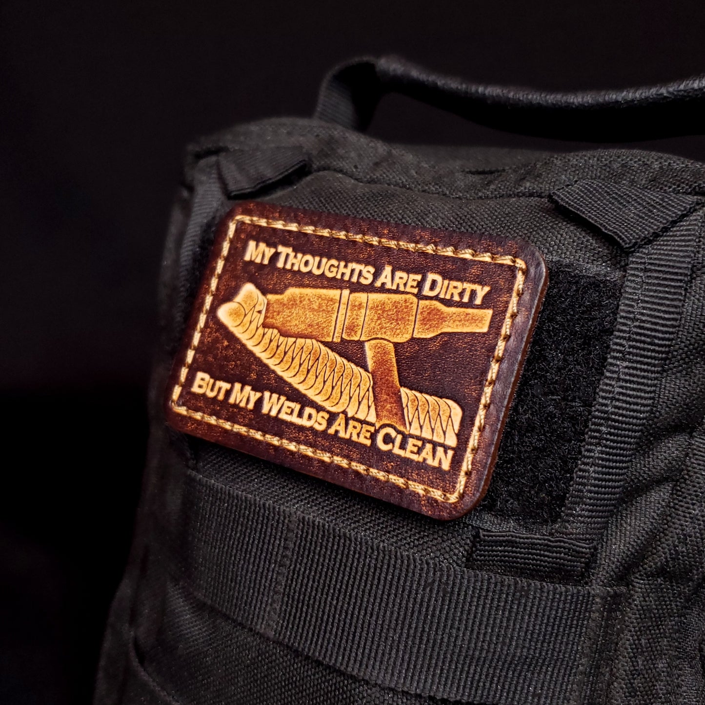 Brown rectangular velcro patch embossed with a picture of a welding tig torch and text, affixed to a bag.