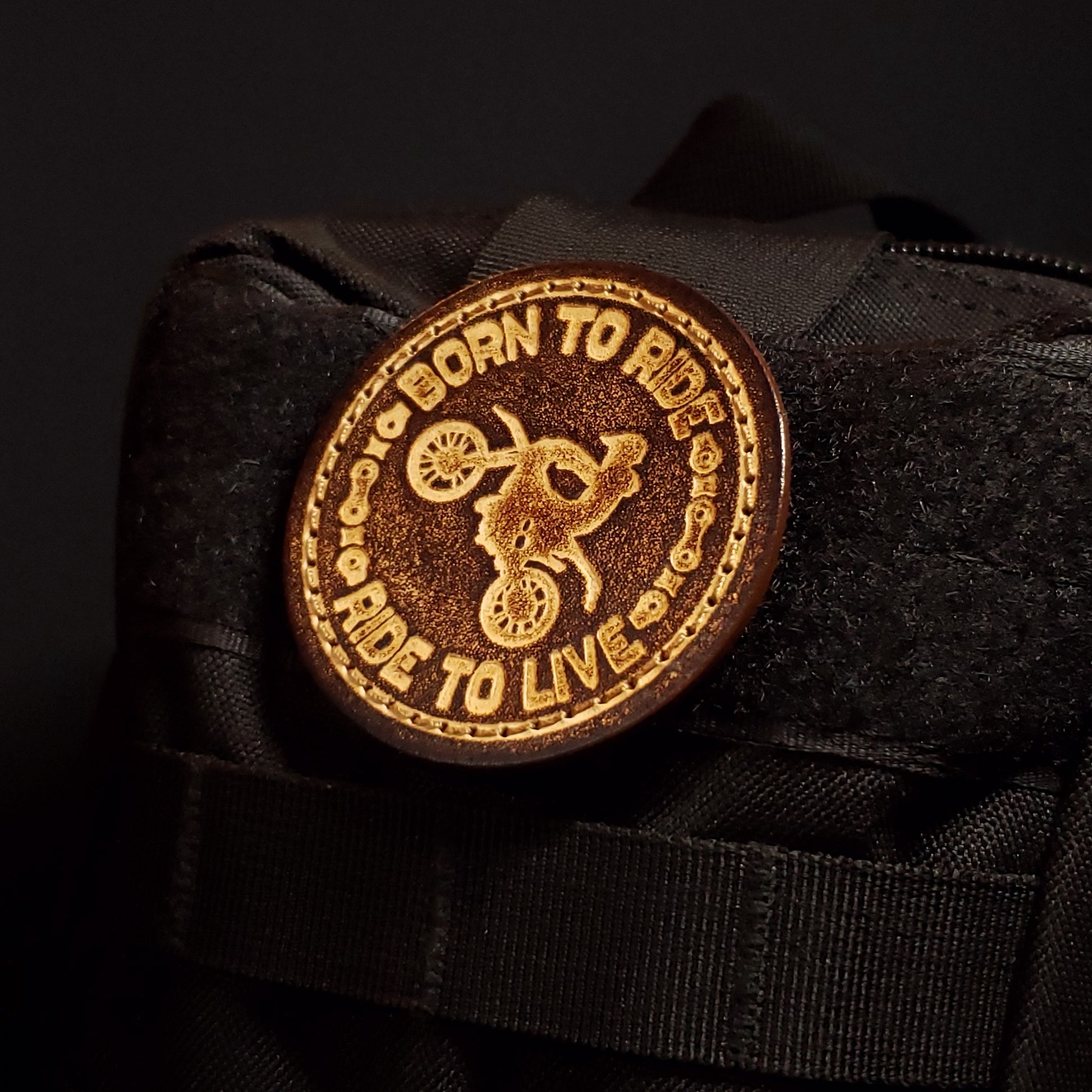 Brown circular velcro patch embossed with text and a graphic of a motorcyclist doing a wheelie, affixed to a bag.