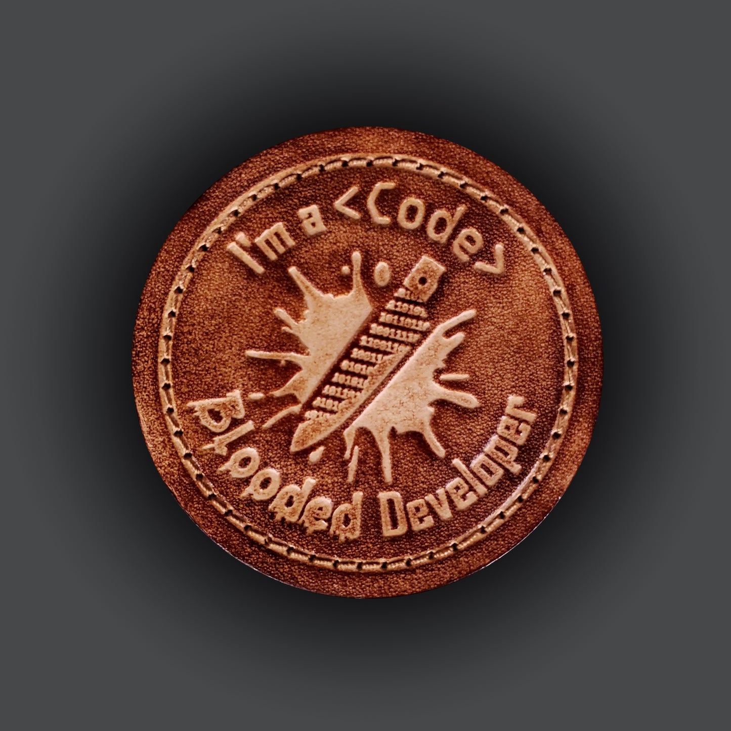Brown leatehr velcro patch featuring text that says "I'm a code blooded developer" and a graphic of a knife made of ones and zeros on a blood splatter.