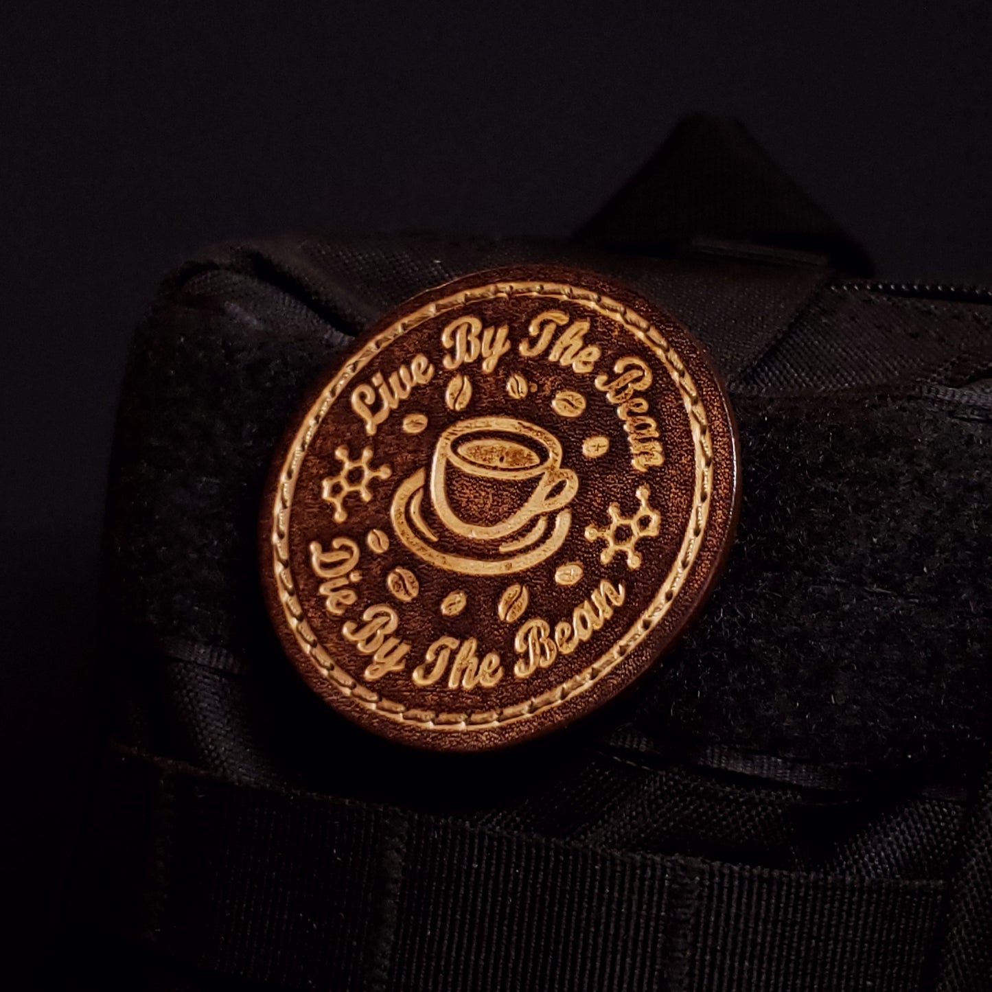 Brown circular velcro patch embossed with coffee themed graphics and text, affixed to a bag.