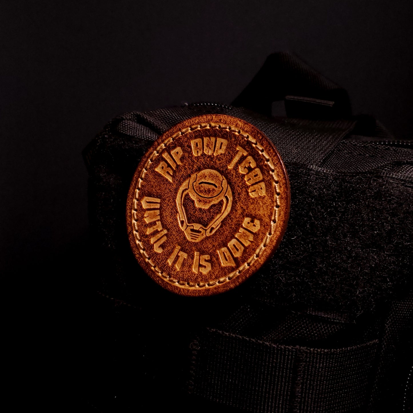 Brown leather velcro patch embossed with text and the Doom slayer's helmet, affixed to a bag.
