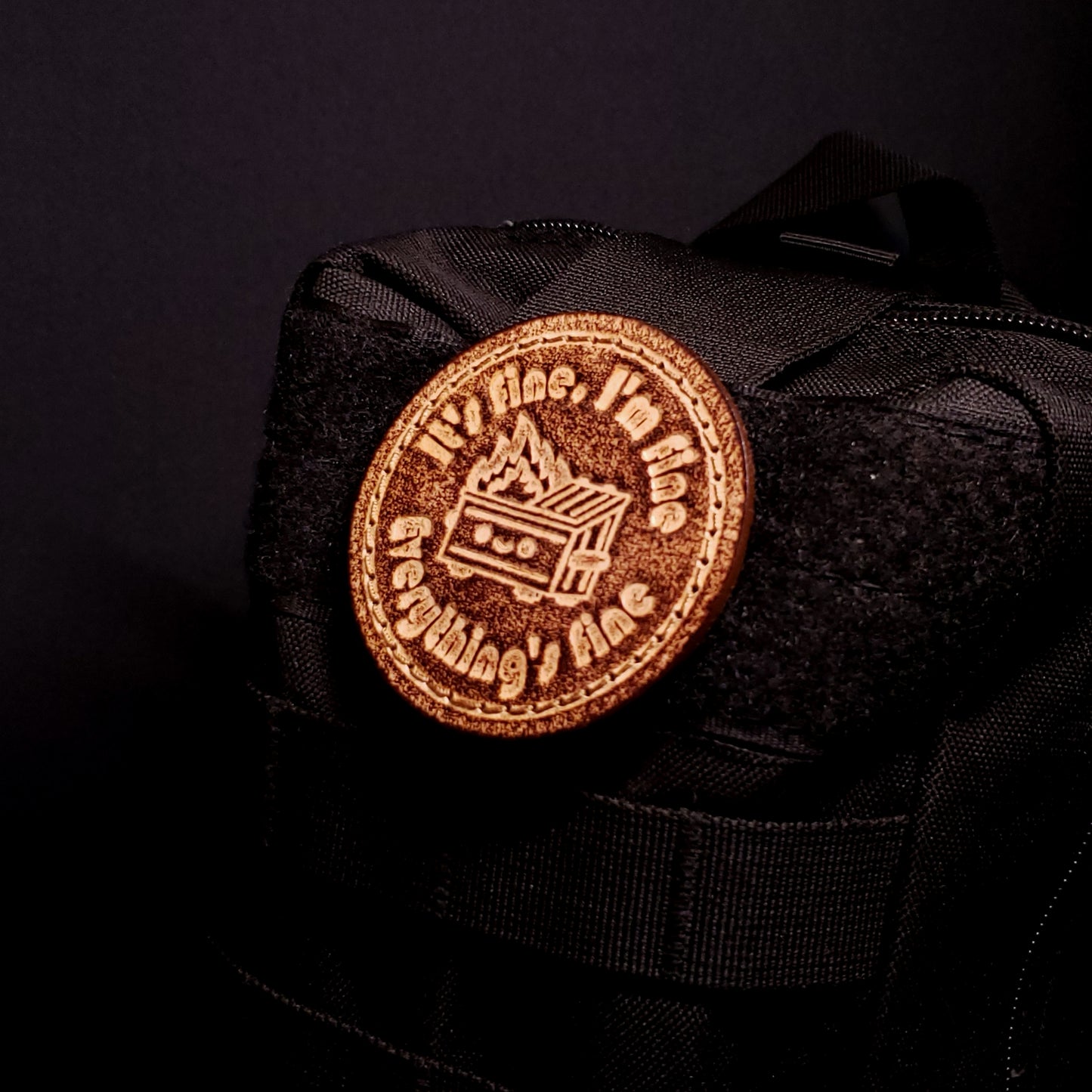 Brown leather velcro patch featuring funny text and a cartoon graphic of a dumpster fire, affixed to a bag.