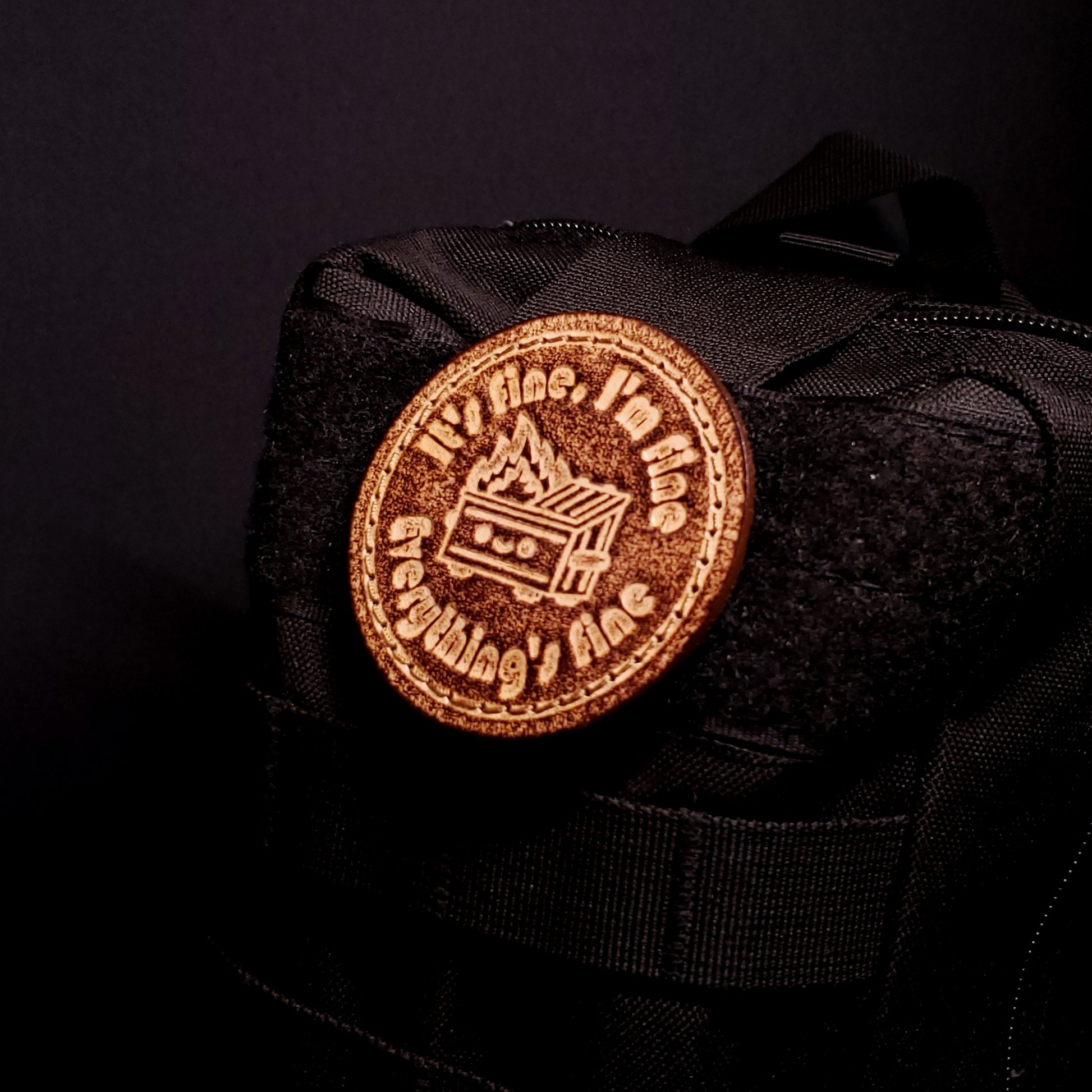 Brown leather velcro patch featuring funny text and a cartoon graphic of a dumpster fire, affixed to a bag.