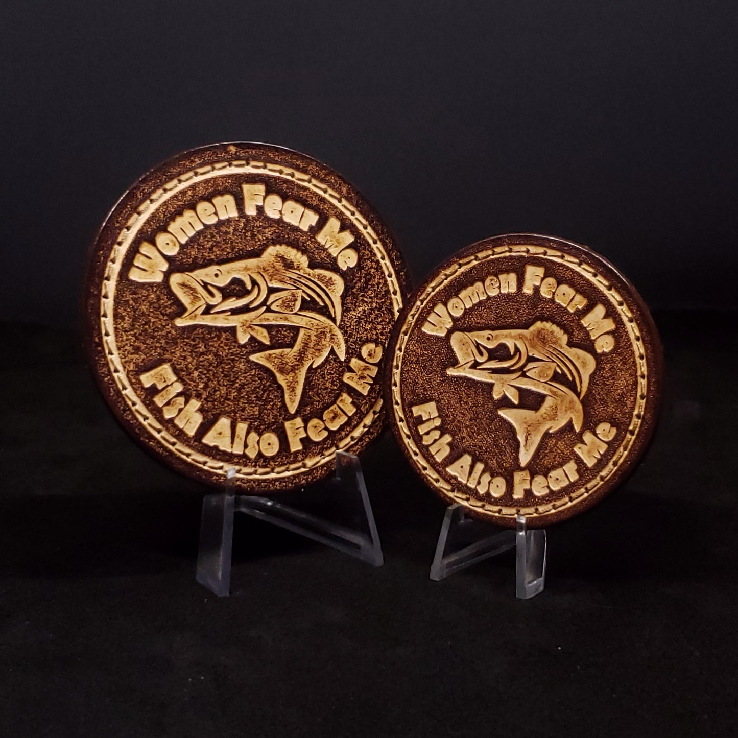 Two brown circular velcro patches embossed with text and a graphic of a fish, posed on a black background.