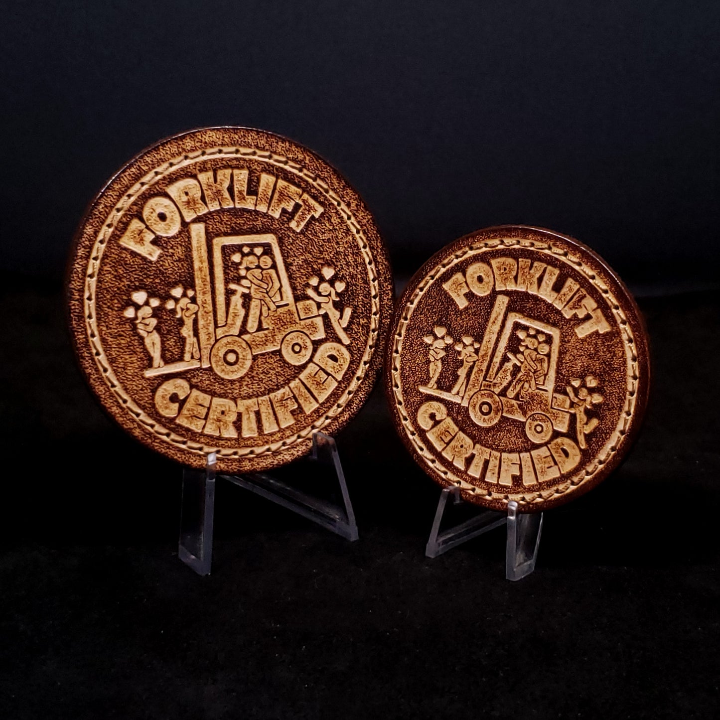 Two brown leather velcro patches embossed with text and a graphic of a man on a forklift surrounded by women who love him.