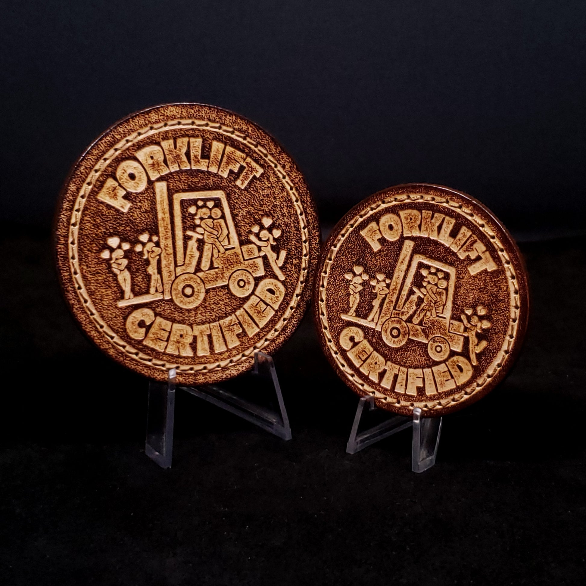 Two brown leather velcro patches embossed with text and a graphic of a man on a forklift surrounded by women who love him.