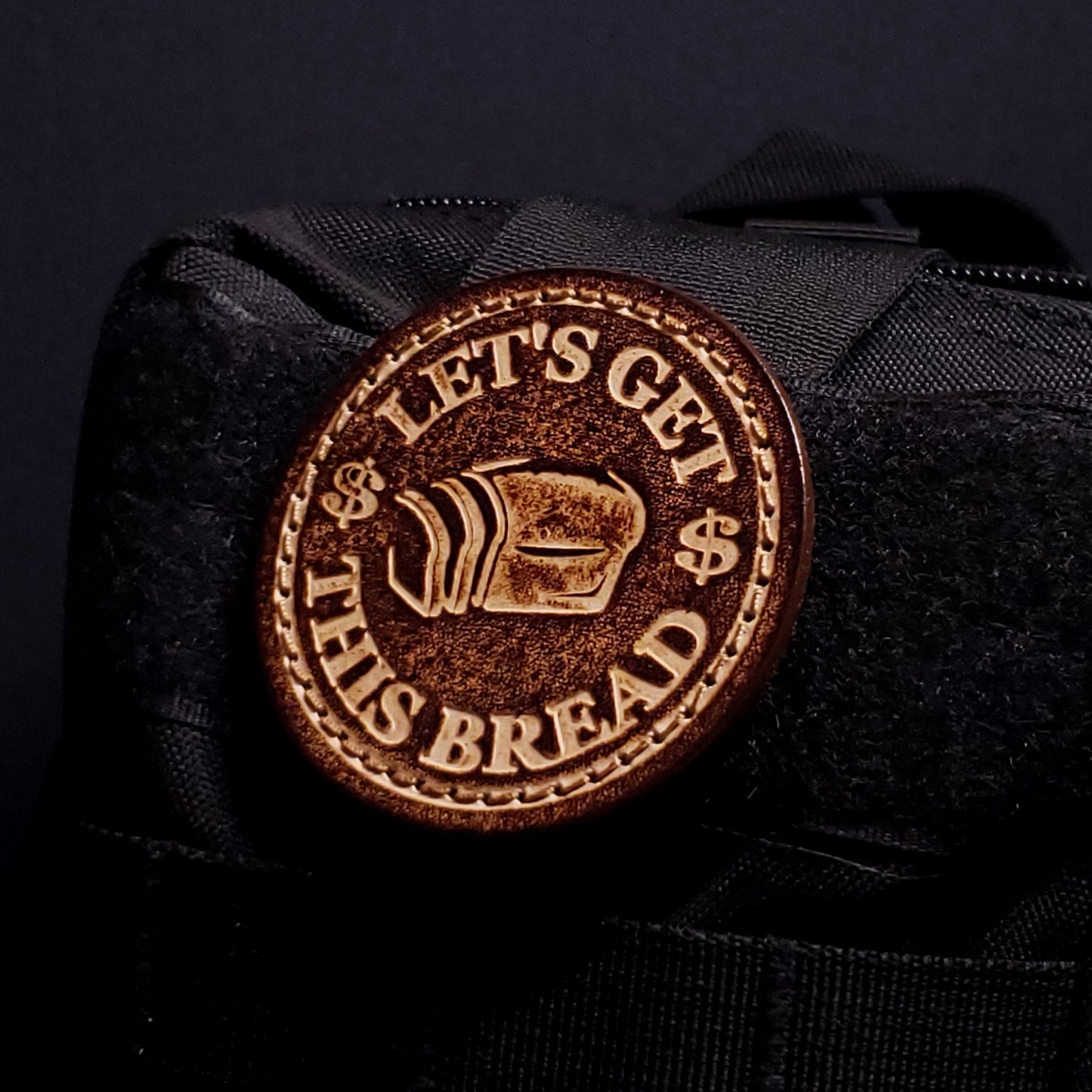 Brown leather velcro patch embossed with text and graphics of slice bread and dollar signs, affixed to a bag.