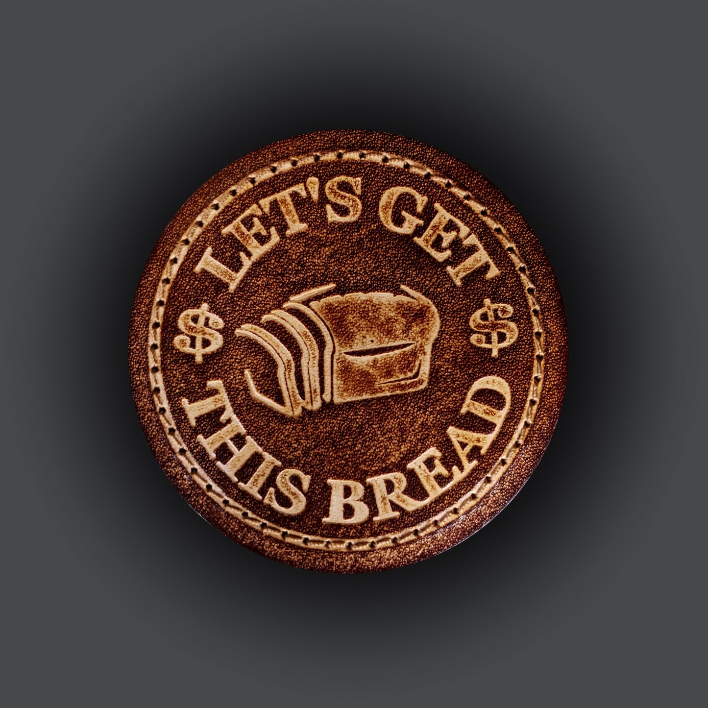 Brown leather velcro patch embossed with a graphic of bread and text that says "Let's get this bread".
