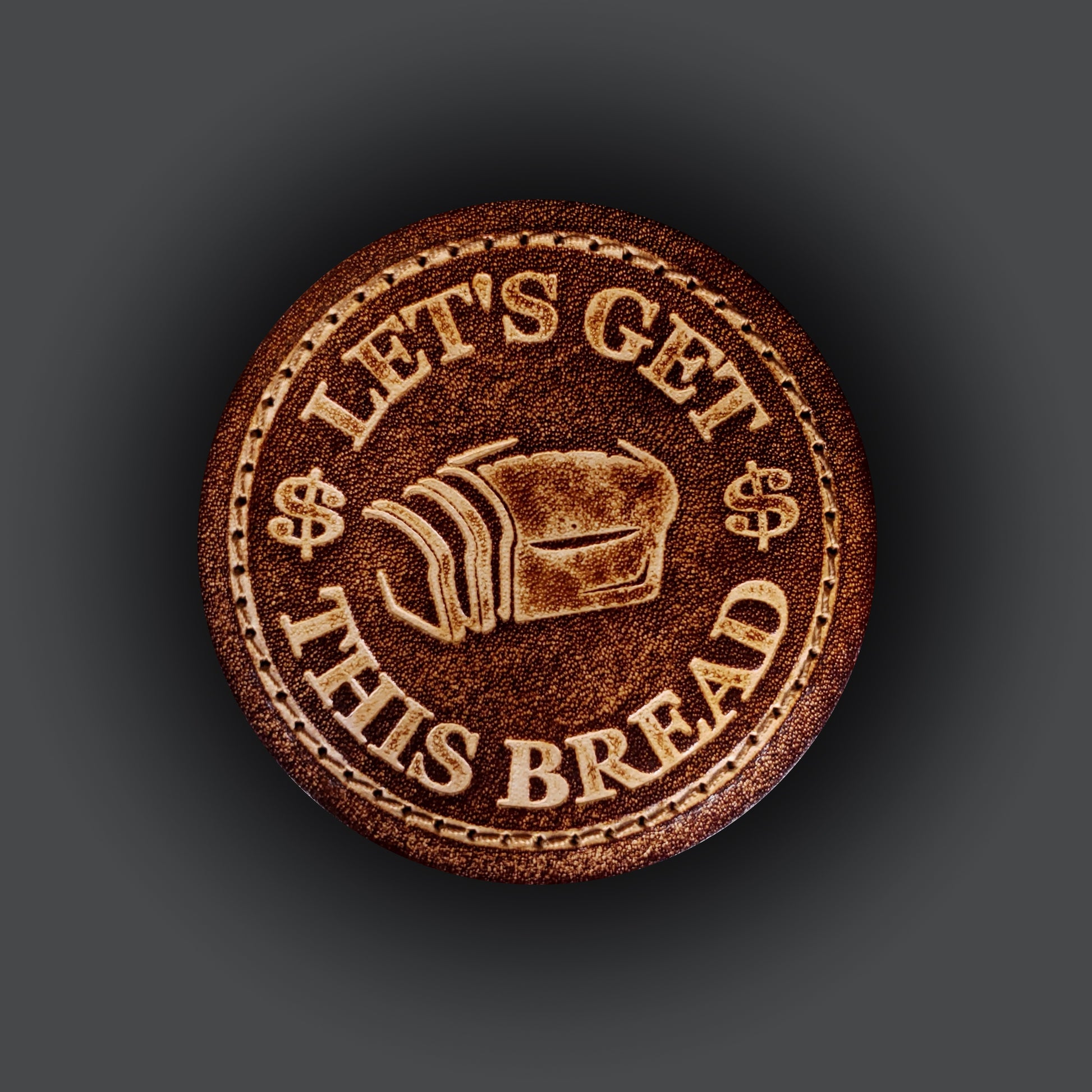 Brown leather velcro patch embossed with a graphic of bread and text that says "Let's get this bread".
