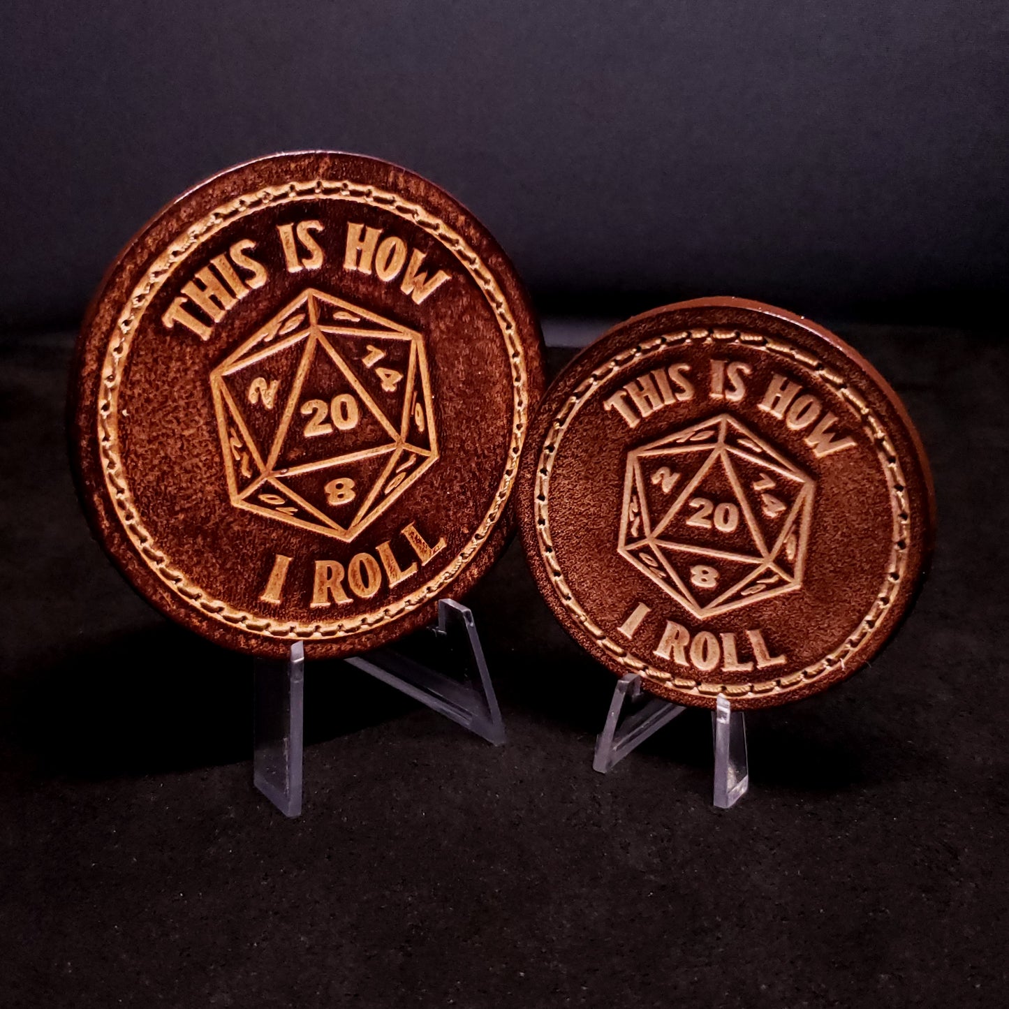 Two brown leather velcro patches with text and an image of a twenty sided die with the number twenty facing up, posed on a black background.