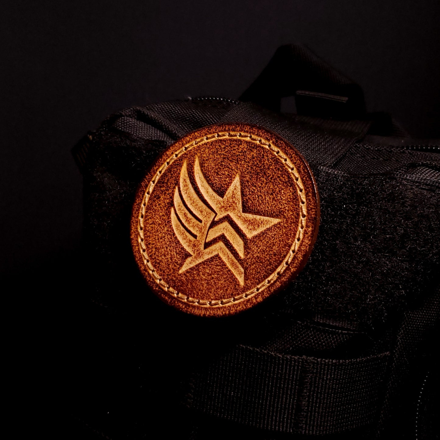 Brown leather velcro patch embossed with a star and wing symbol from the Mass Effect franchise, affixed to a bag.