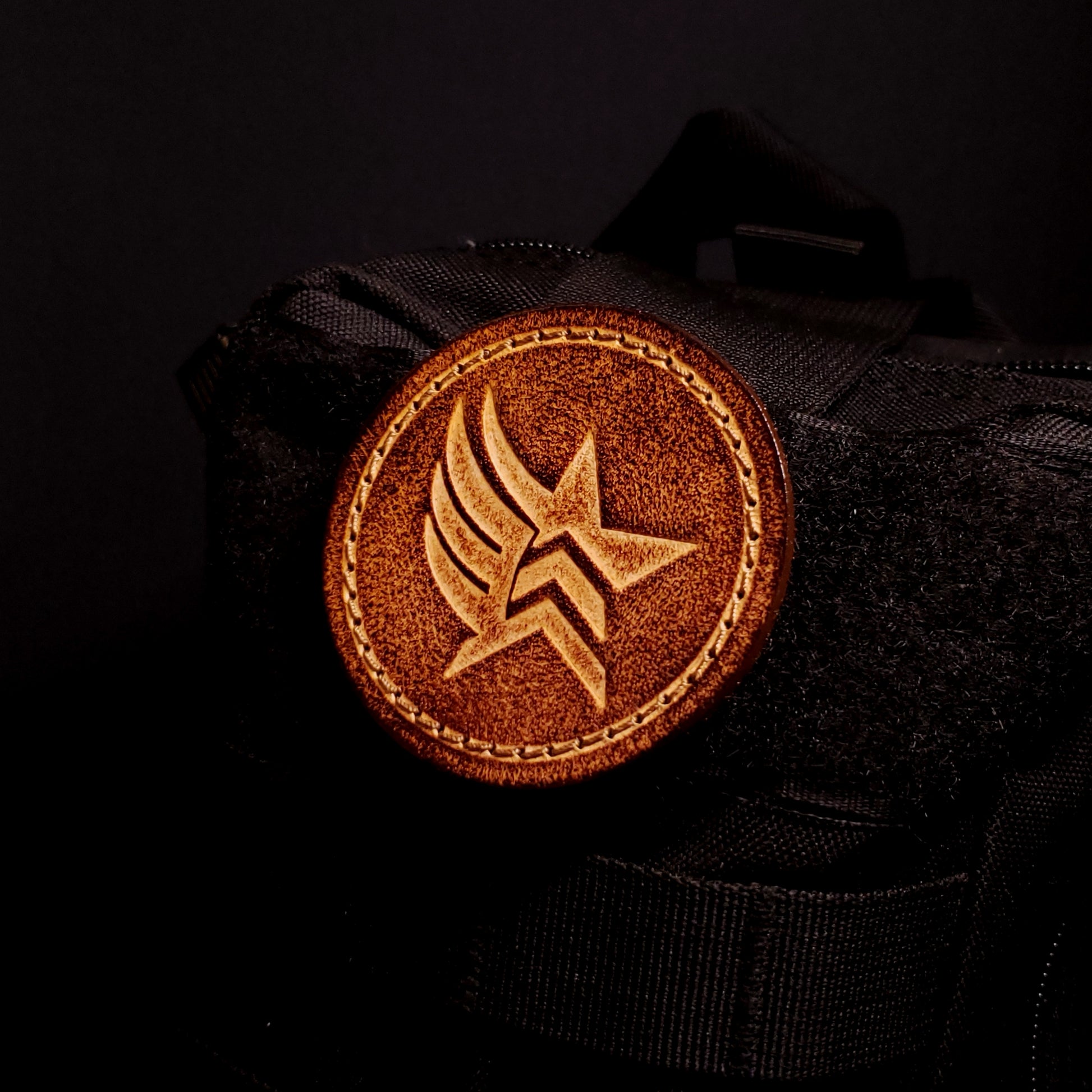 Brown leather velcro patch embossed with a star and wing symbol from the Mass Effect franchise, affixed to a bag.