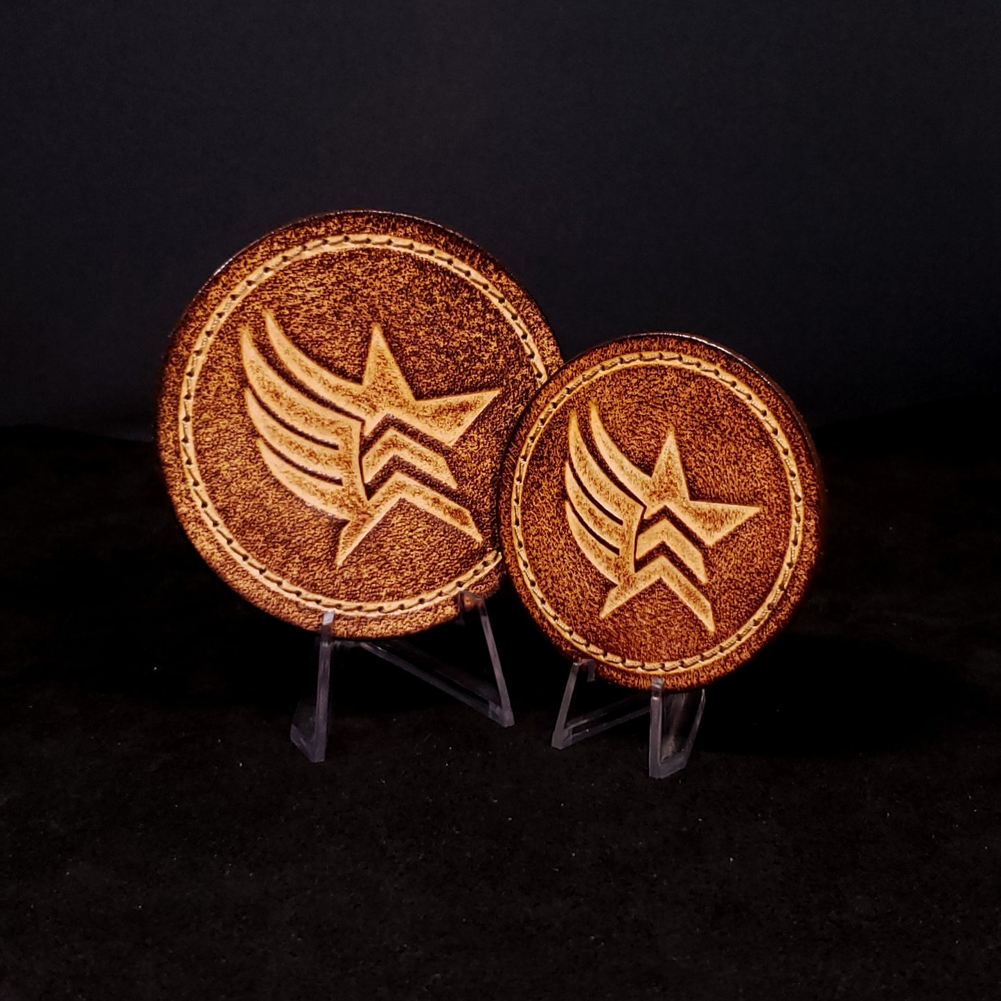 Two brown leather velcro patches embossed with a star and wing symbol from the Mass Effect franchise, posed on a black background.