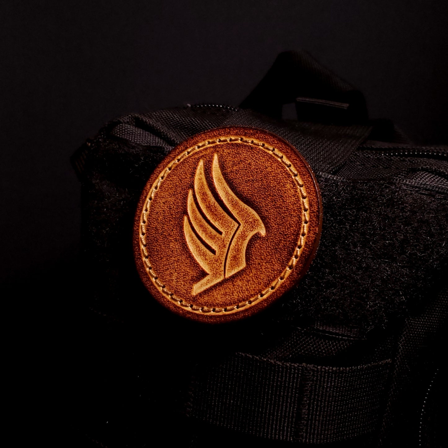 Brown leather velcro patch embossed with a wing symbol from the Mass Effect franchise, affixed to a bag.