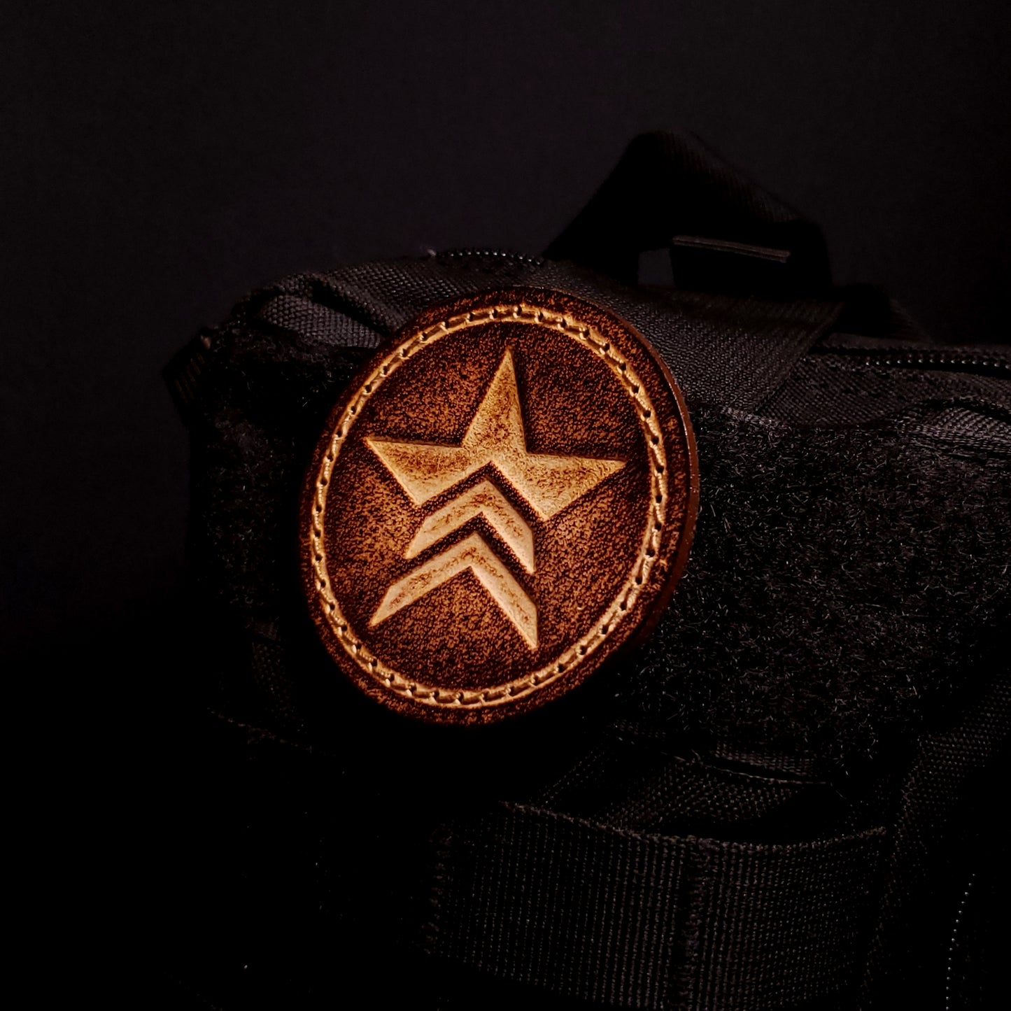 Brown leather velcro patch embossed with a star symbol with chevrons from the Mass Effect franchise, affixed to a bag.