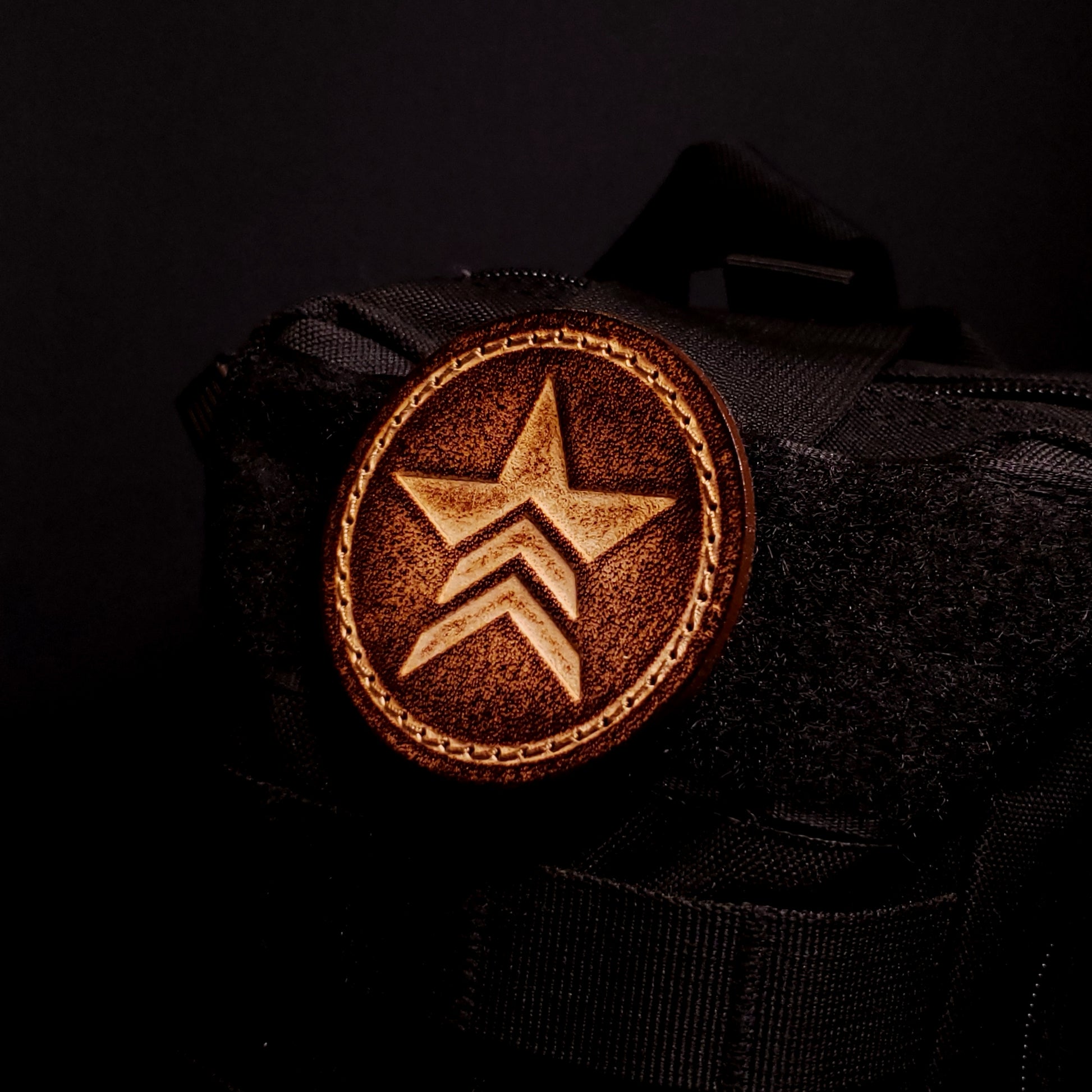 Brown leather velcro patch embossed with a star symbol with chevrons from the Mass Effect franchise, affixed to a bag.
