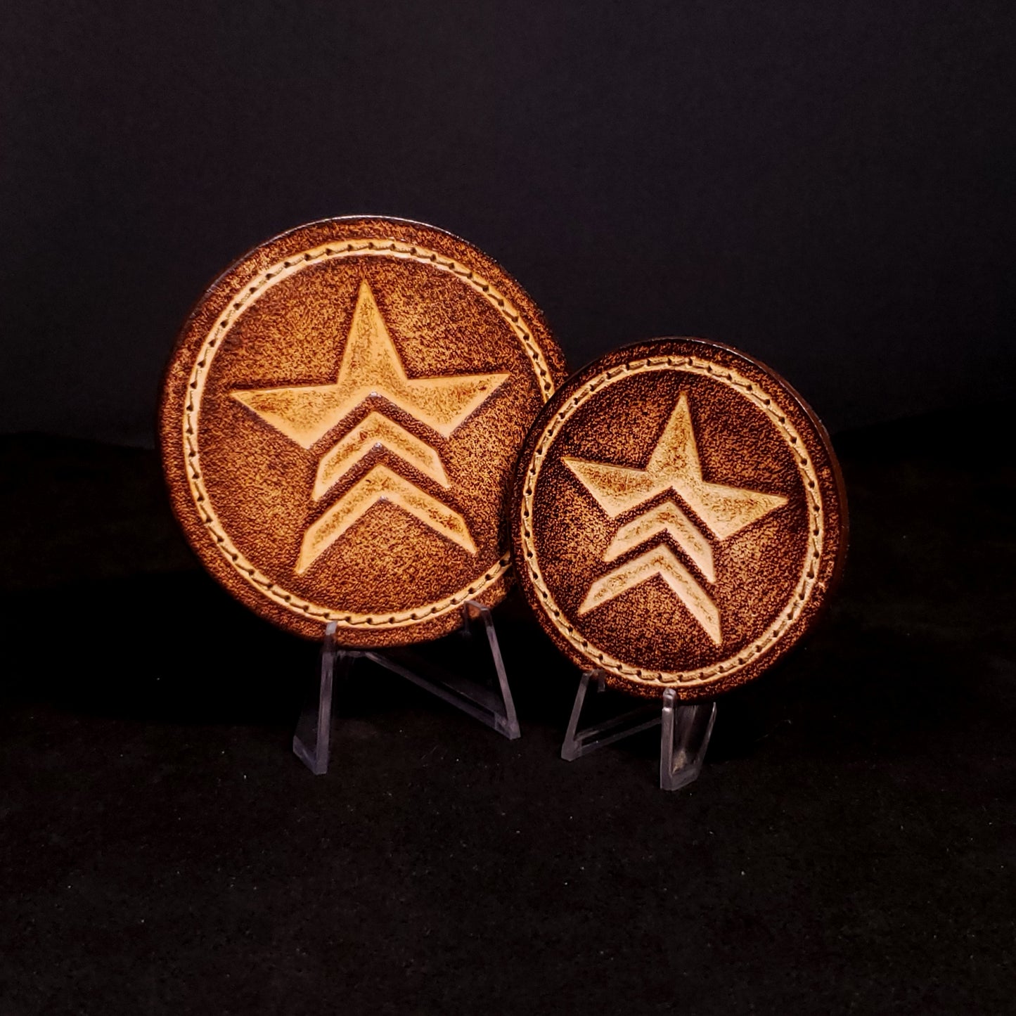 Two brown leather velcro patches embossed with a star symbol with chevrons from the Mass Effect franchise, posed on a black background.