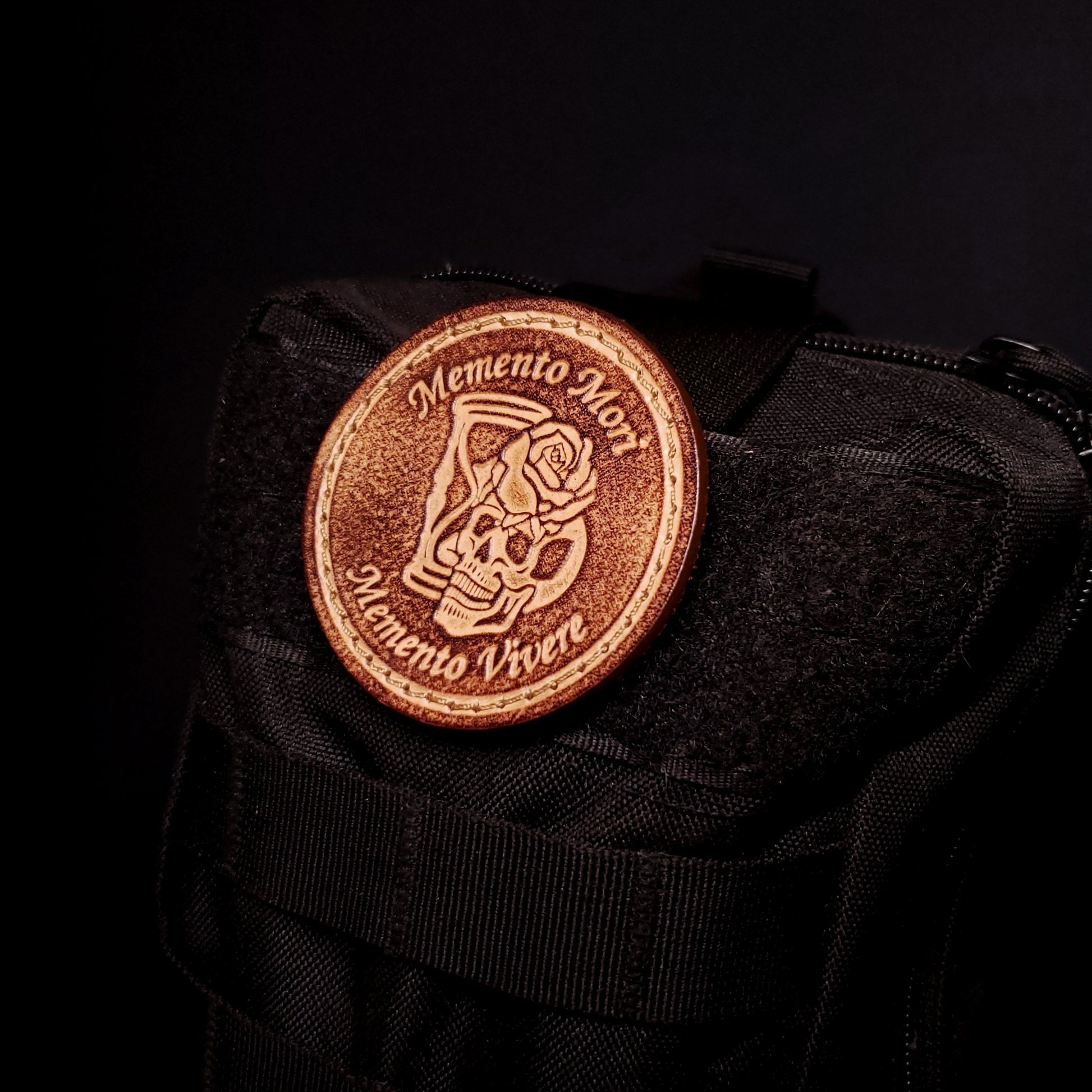 Brown leather velcro patch with text that says an image of a skull, rose, and hourglass, affixed to a bag.
